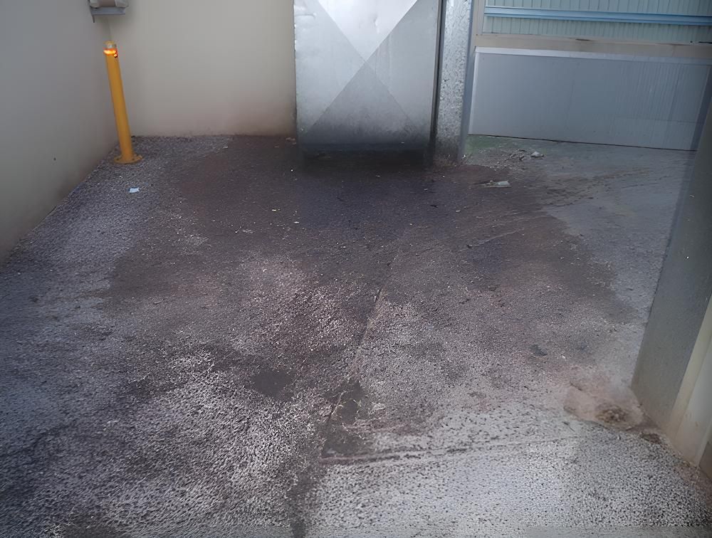 A Dirty Concrete Floor With A Metal Door In The Background — EcoPro Pressure Cleaning In Logan, QLD