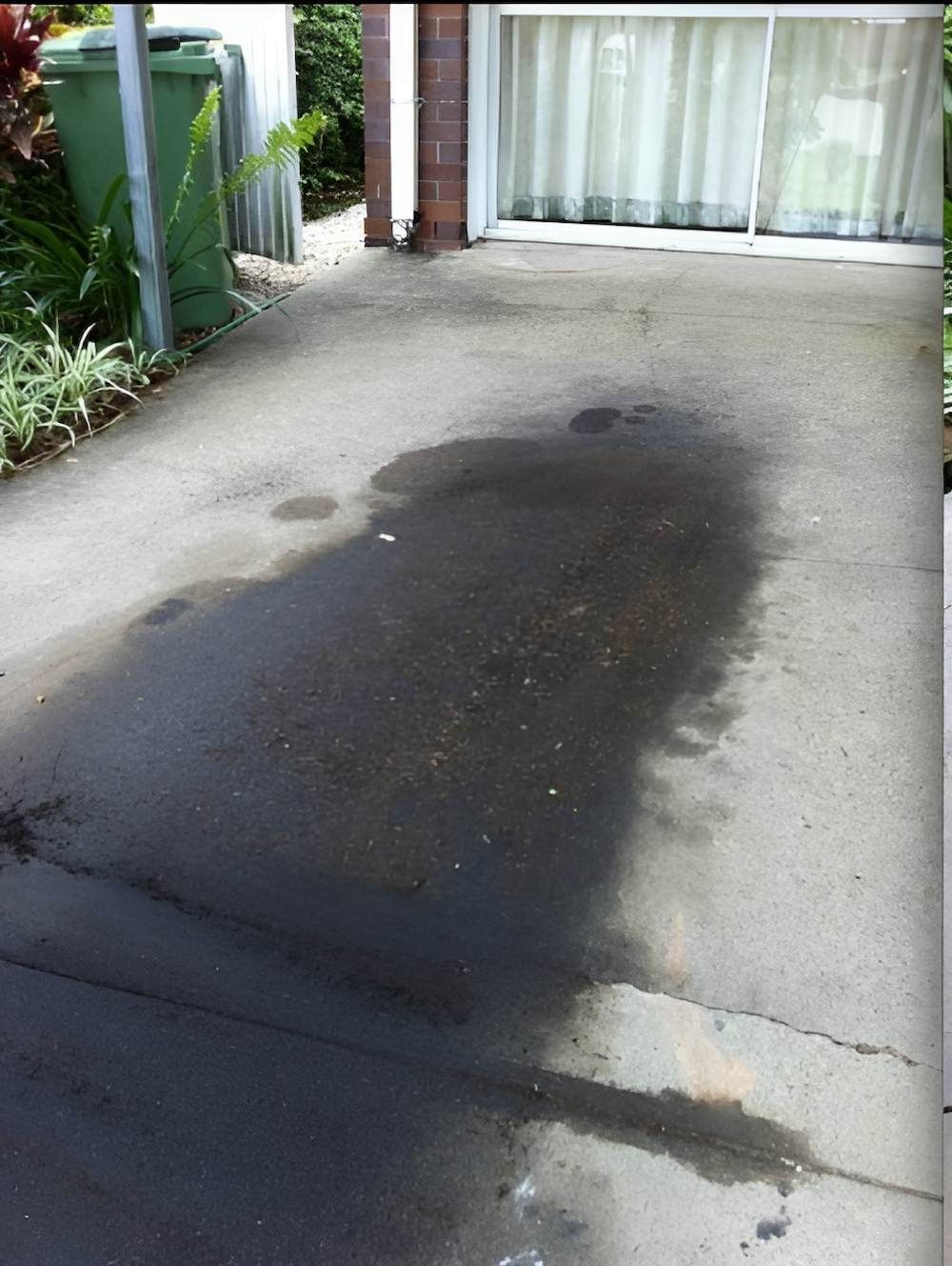 A Dirty Driveway With A Green Trash Can In The Background — EcoPro Pressure Cleaning In Coolangatta, QLD