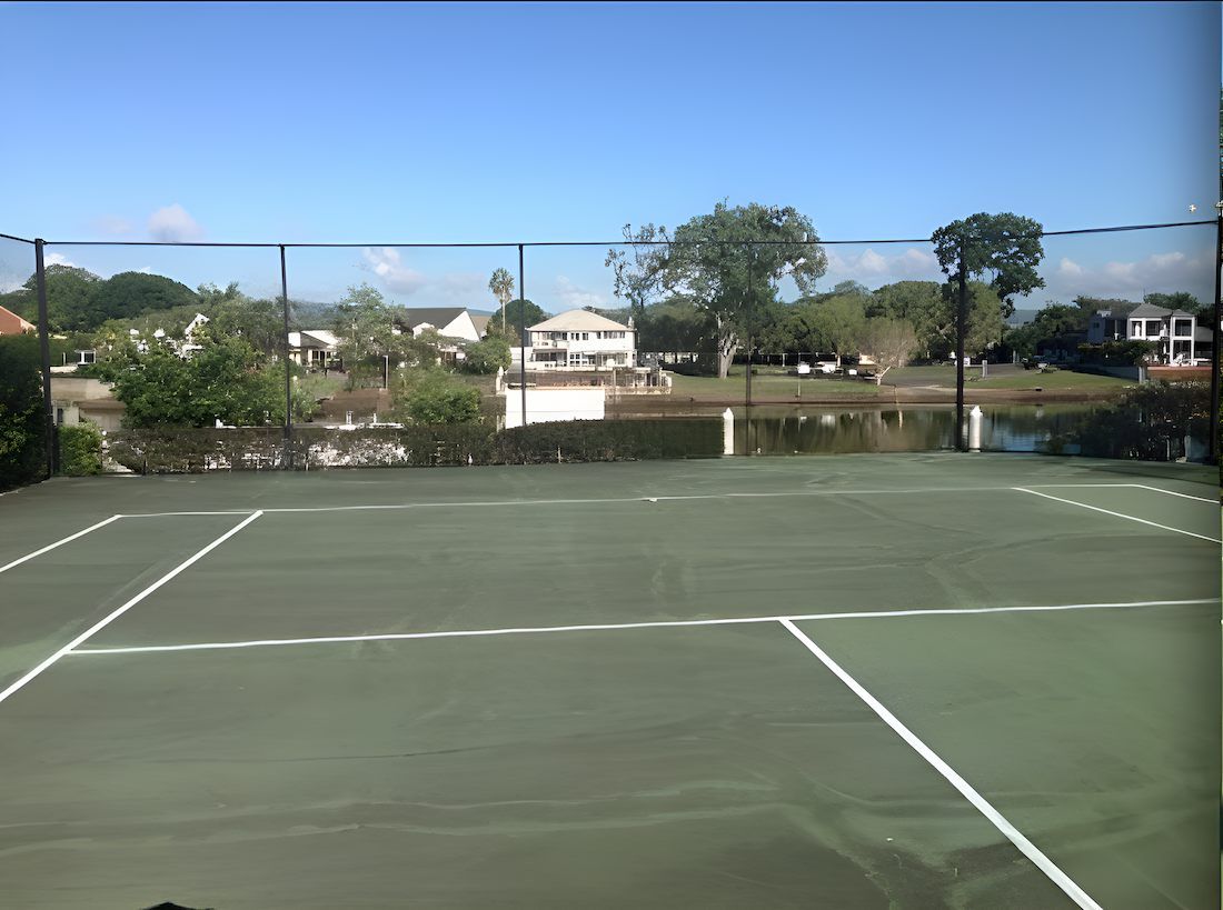 A Tennis Court With A Fence Around It And A Pond In The Background — EcoPro Pressure Cleaning In Southport, QLD