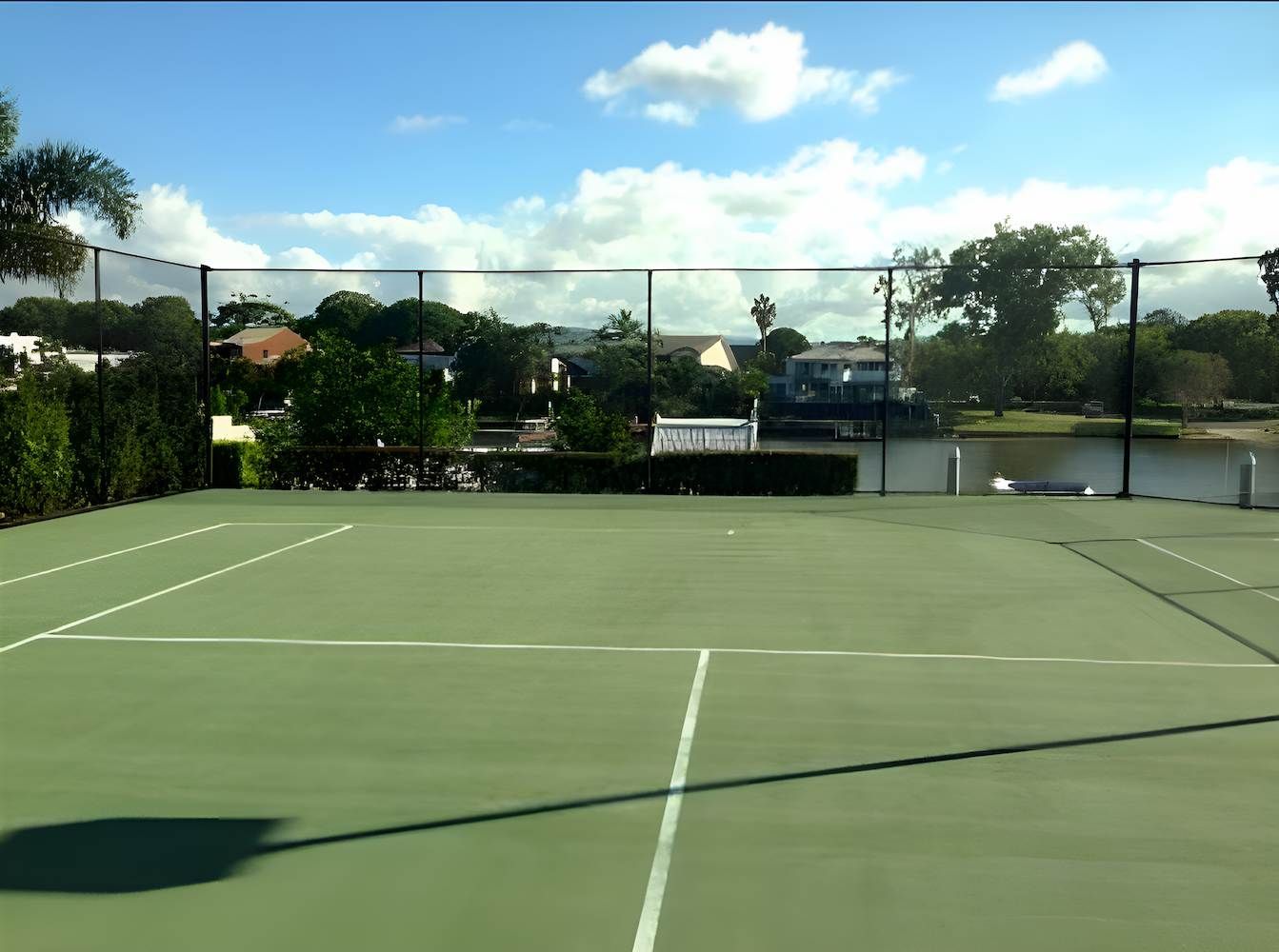 A Tennis Court With A Fence Around It And A Lake In The Background — EcoPro Pressure Cleaning In Broadbeach, QLD