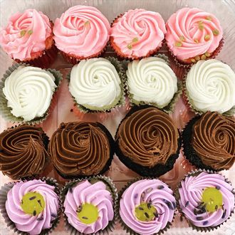 Assorted frosted cupcakes with pink, white, brown, and lavender swirls arranged in rows.
