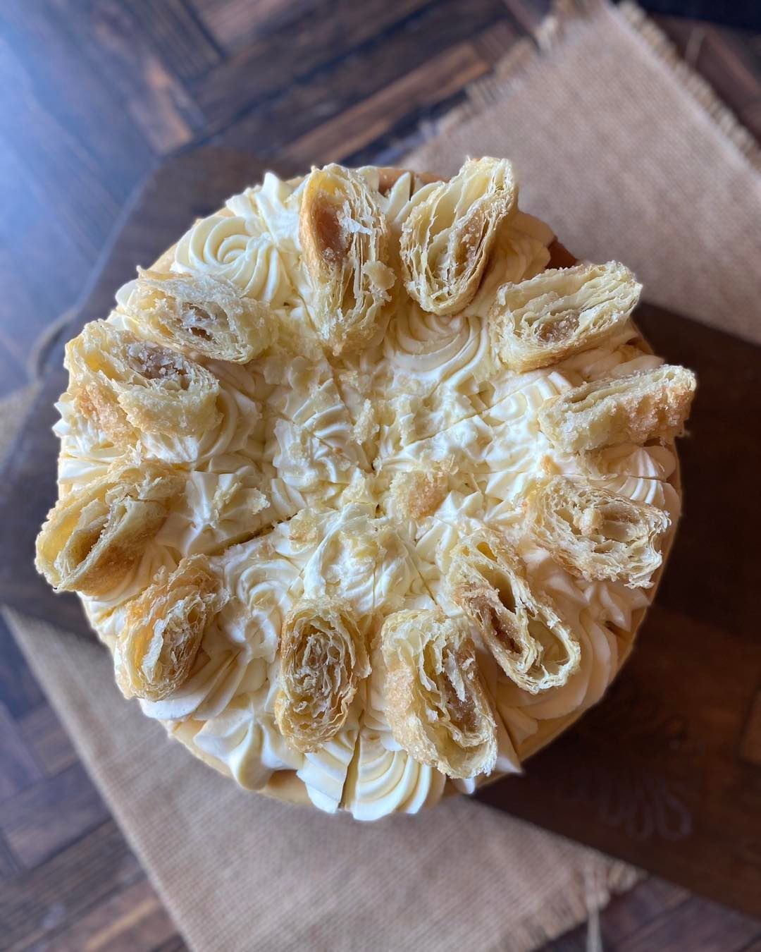 Top view of a round frosted cake topped with toasted coconut flakes on a wooden board