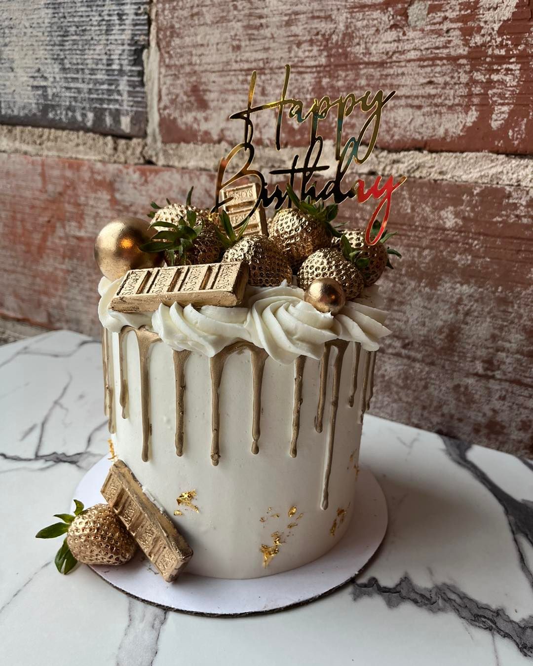 White drip cake with gold accents, Christmas topper, and gold ornaments on a marble surface