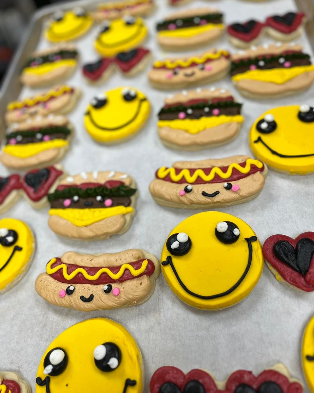Smiley face and hot dog cookies with yellow, red, and black icing on a tray