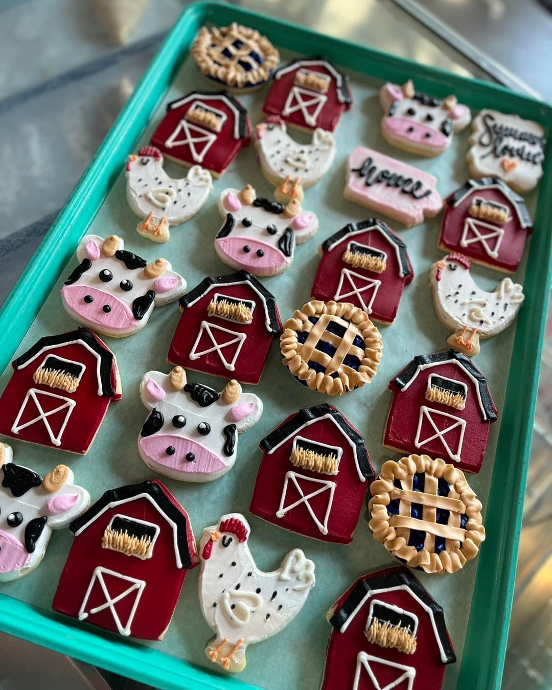 Tray of farm-themed decorated cookies with red barns, cows, chickens, and pie designs