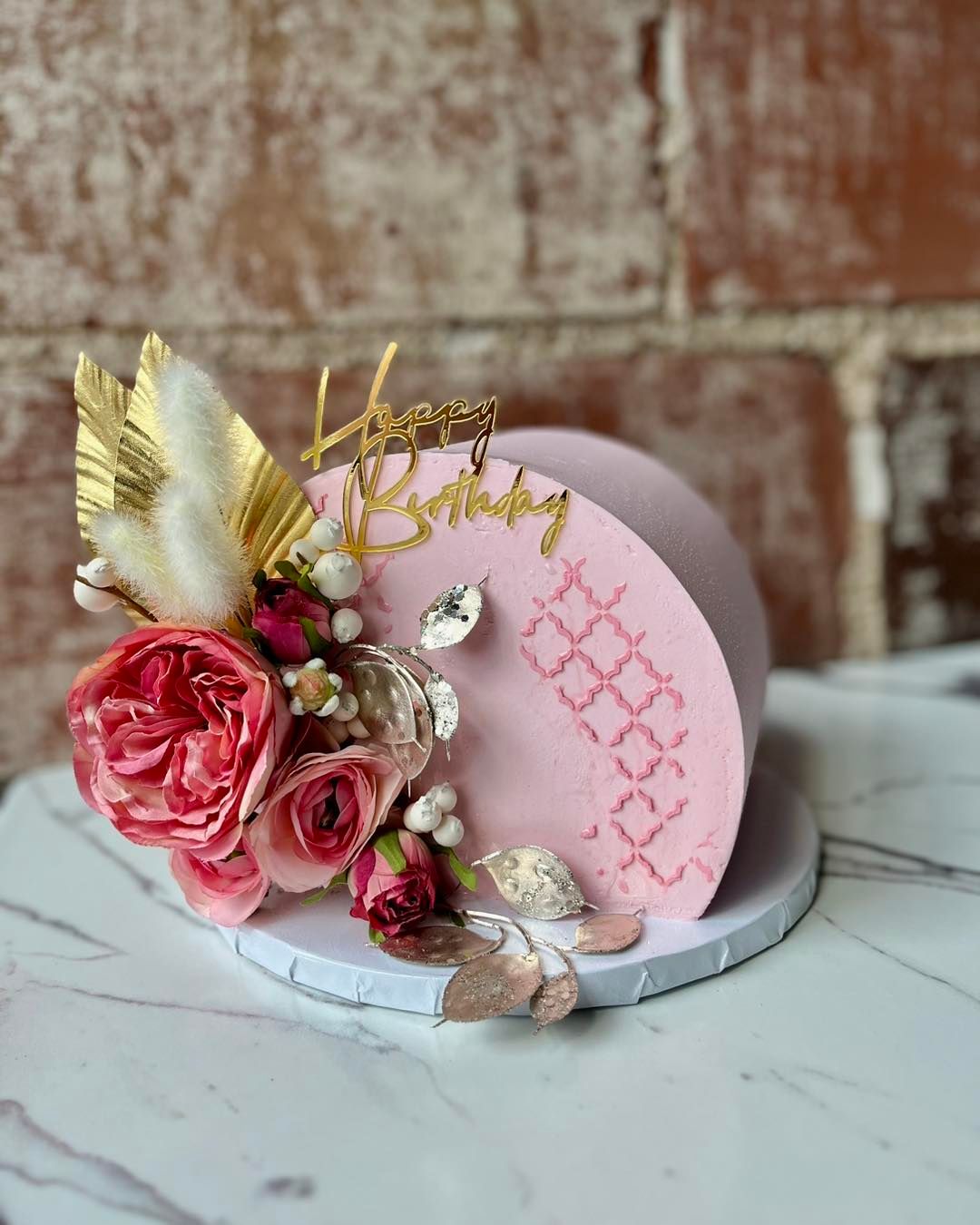 Pink floral cake with gold accents and “Happy Birthday” topper on a white stand