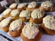 Tray of small iced cupcakes or muffins with white frosting, arranged in rows on a table.