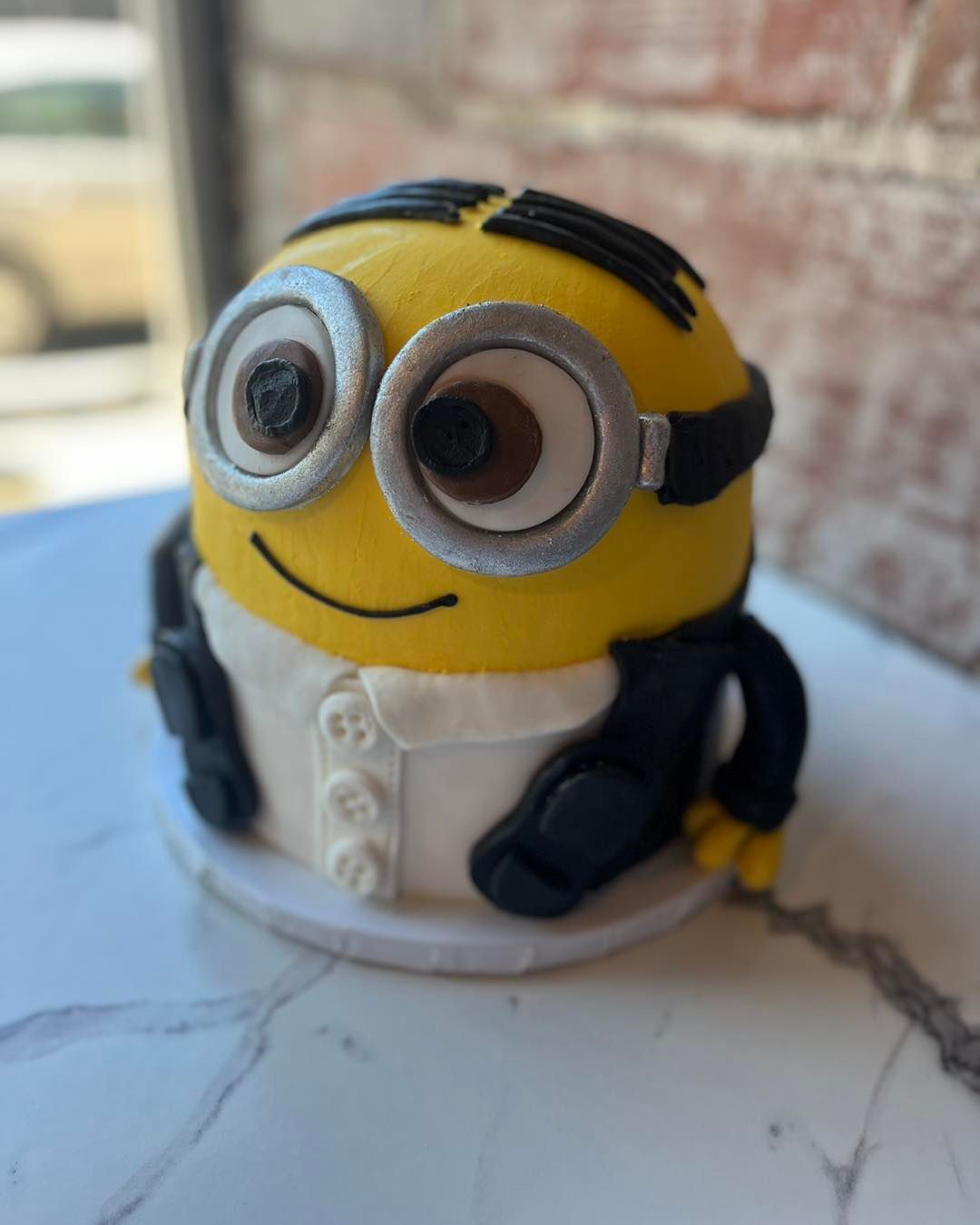 Minion figurine in a white outfit on a marble surface, smiling with large goggles.