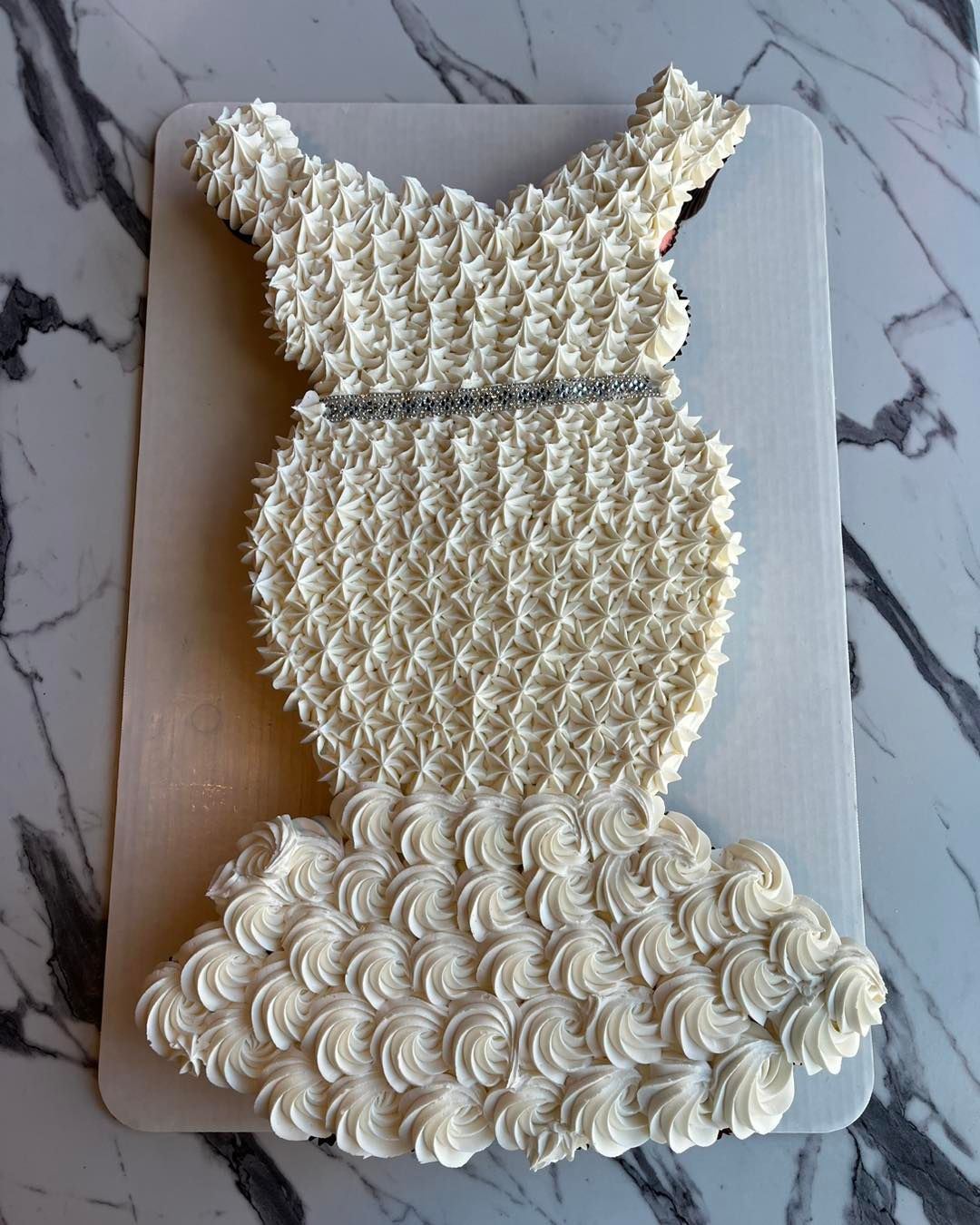 White textured cake shaped like a dress, decorated with rosette frosting on a marble board.