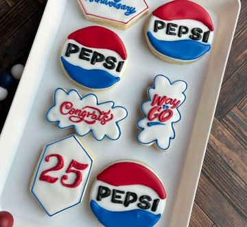Pepsi-themed royal icing cookies in red, white, and blue on a tray, including a “25” cookie and logos.