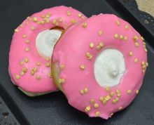 Two pink signature champagne donuts with white centers and yellow sprinkles on a dark surface
