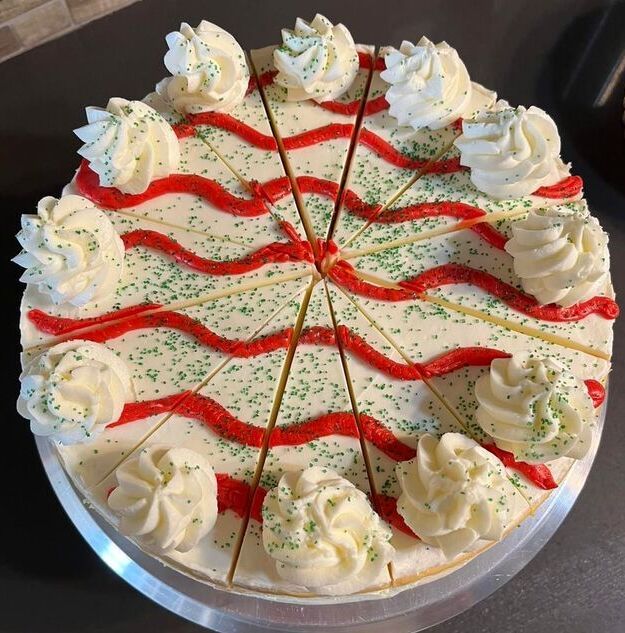Round cake with white frosting, red swirls, green sprinkles, and piped rosettes on a silver tray