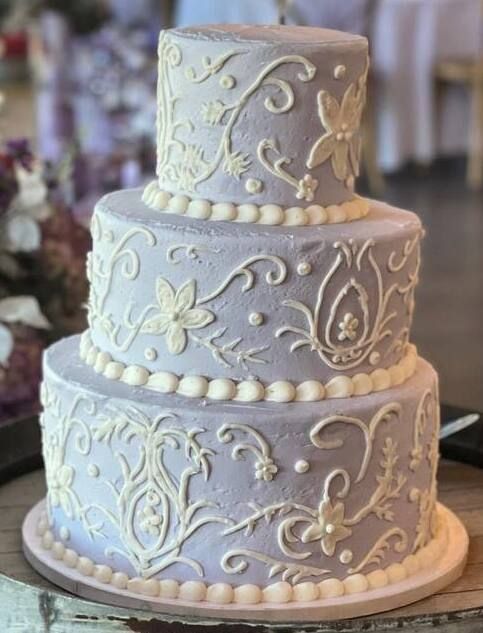 Three-tier white wedding cake with ivory floral piping and pearl border on a plate