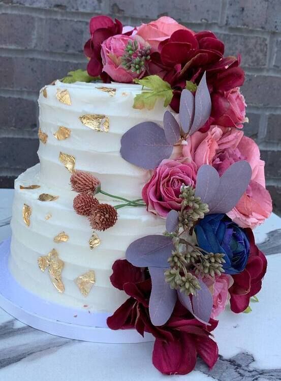 White cake with gold accents and pink, purple, and blue floral decorations on the side