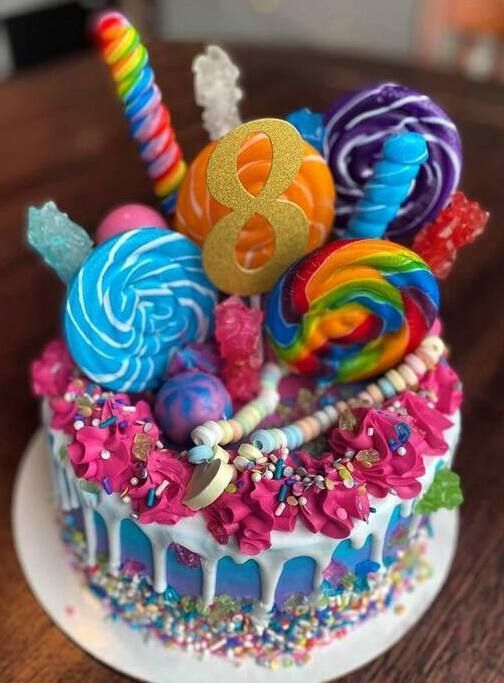 Colorful candy-covered birthday cake with lollipops and rainbow frosting on a table
