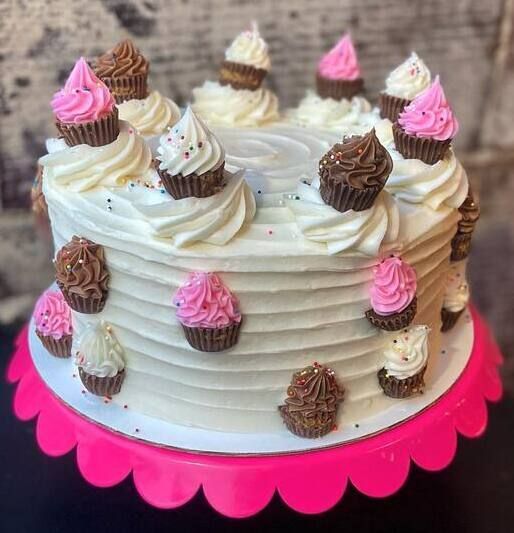 White frosted cake with pink and chocolate mini cupcakes, on a bright pink scalloped stand