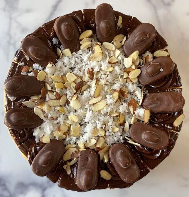 Chocolate-topped dessert with sliced almonds and shredded coconut on a white marble surface