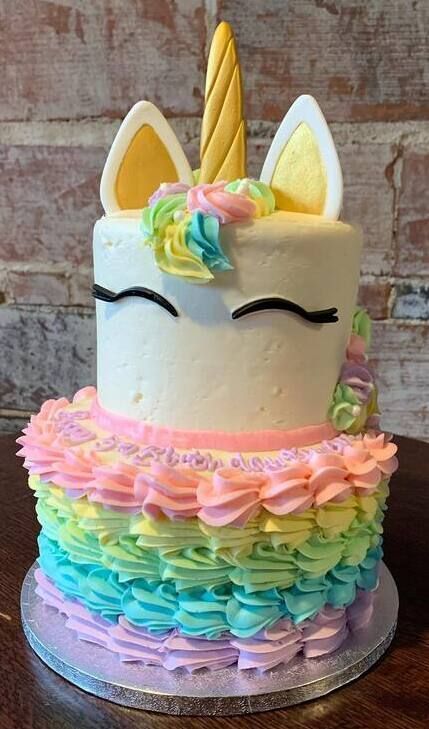 Unicorn-themed pastel cake with rainbow ruffles, closed eyes, ears, and a gold horn