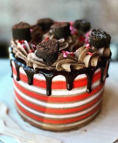 Red-striped cake topped with chocolate drizzle, cream swirls, and chocolate cake pieces on a white stand