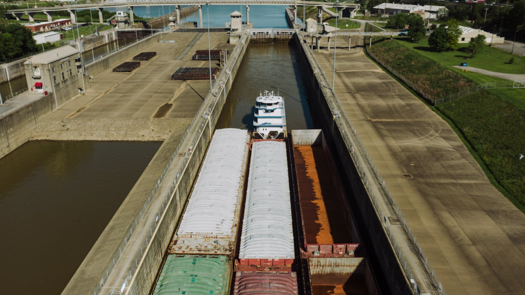 Barge navigating a lock system; brown and white boats in a concrete channel with green banks and blue water.