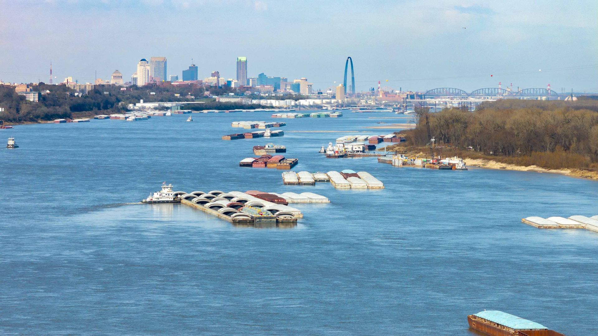 City skyline and river with floating ice, boats, and a snowy shoreline on a clear day