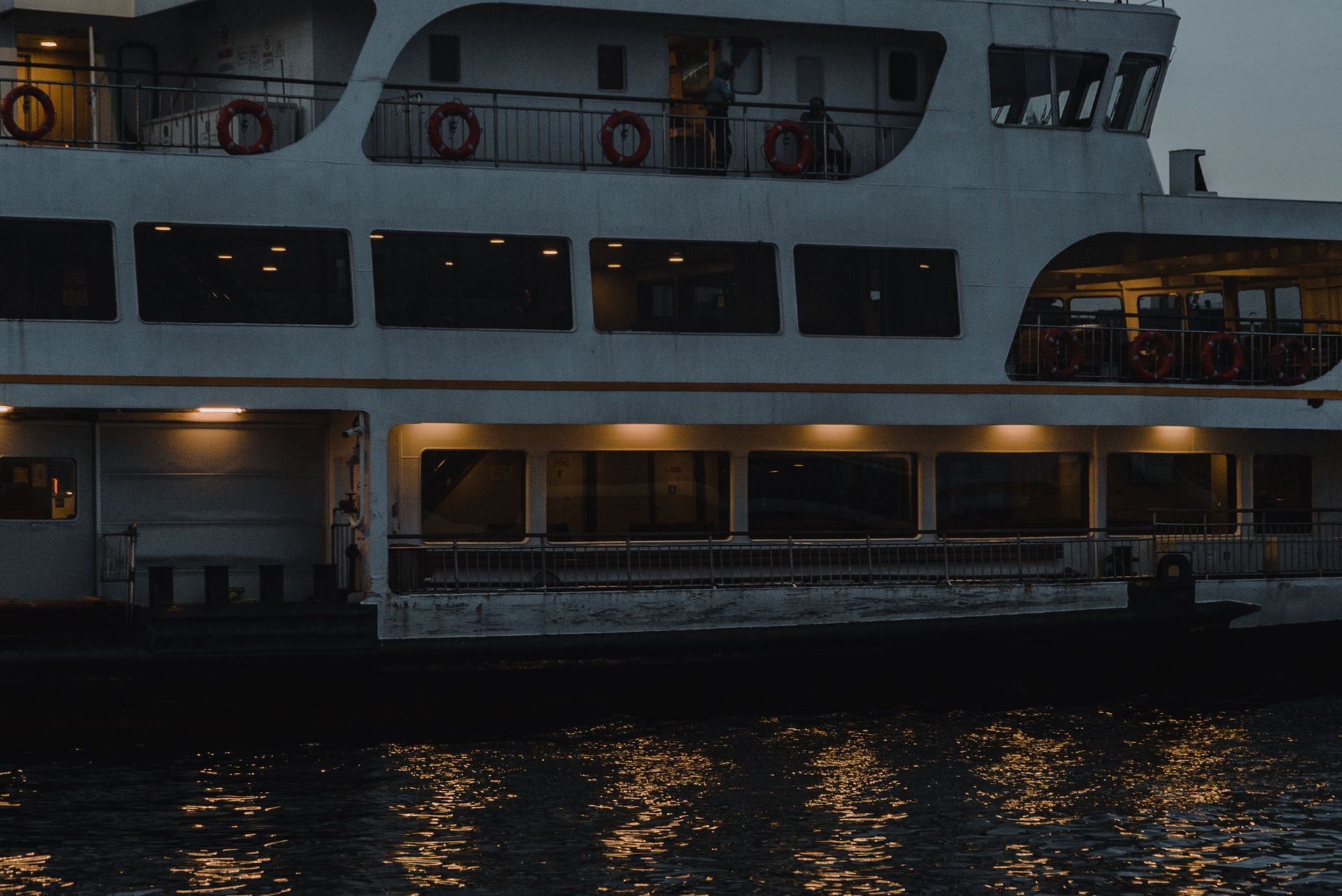 Large white ferry docked at dusk, with lit windows reflecting on dark water