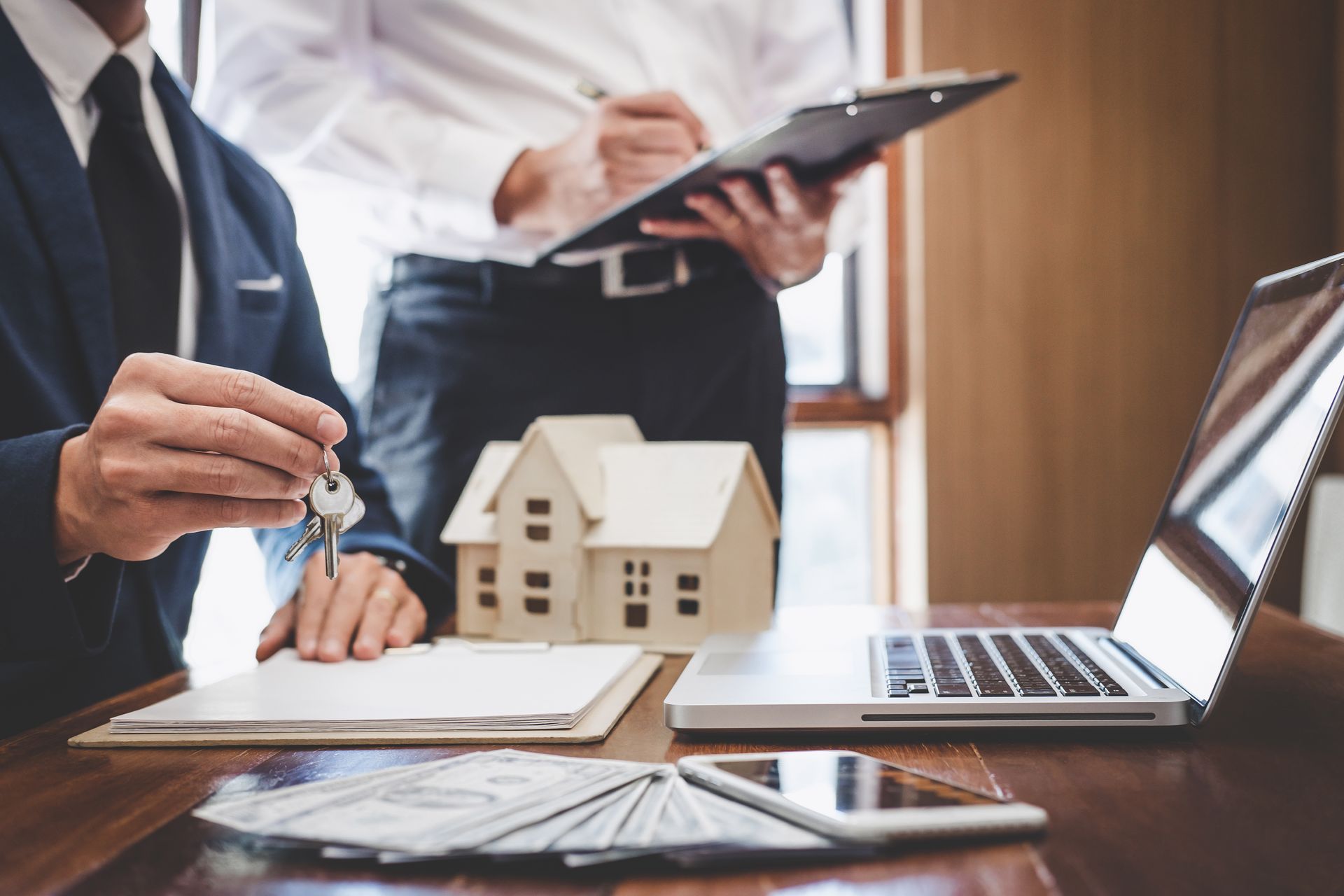 Business meeting with clipboard, laptop, and small house model on a desk