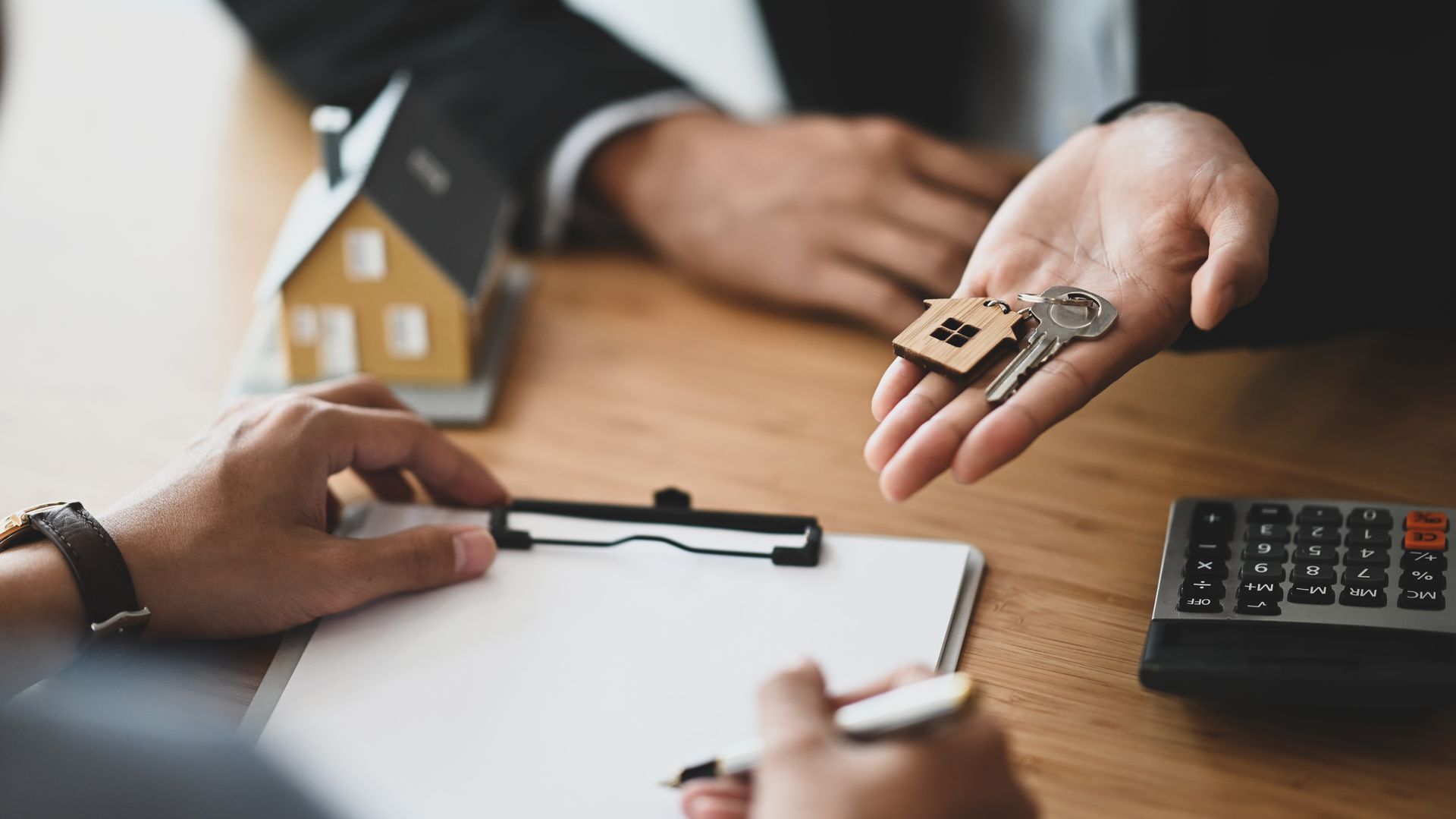Hand holding house keys over a desk during a property signing, with documents and calculator nearby