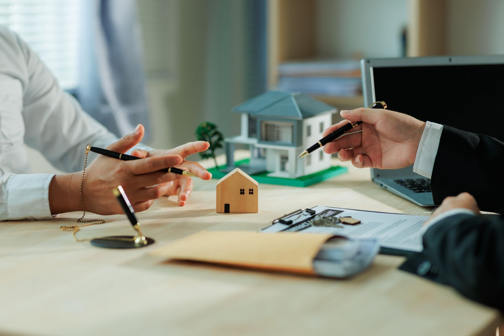 Business meeting with hands gesturing over a house model and laptop on a desk