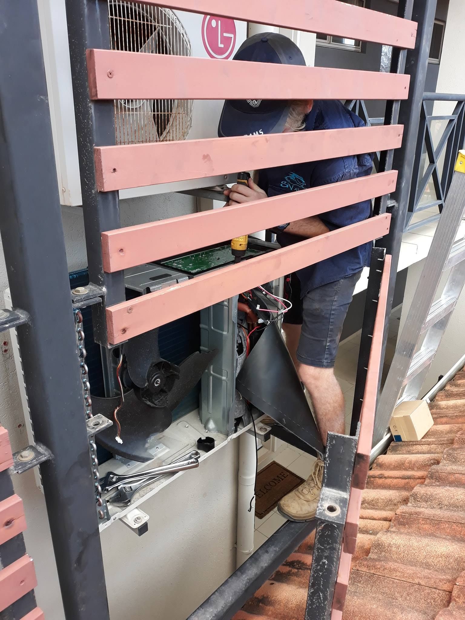 A man is working on an air conditioner behind a fence.