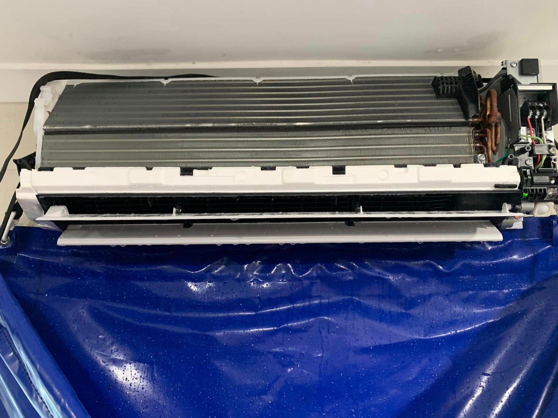 A white air conditioner is sitting on top of a blue plastic bag ready for a hydro clean