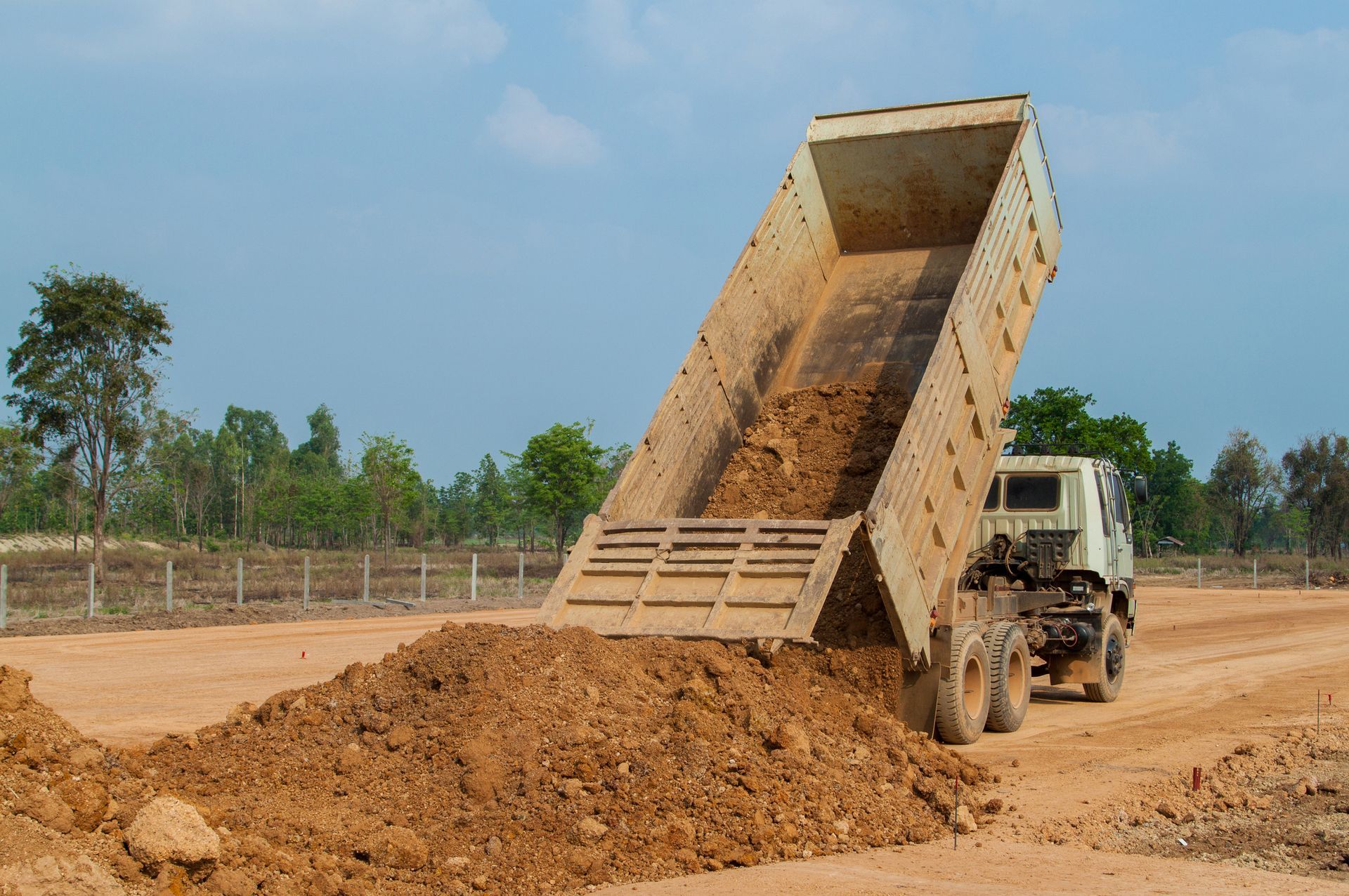 A dump truck is dumping dirt on a dirt road. A dump truck is dumping dirt on a dirt road.