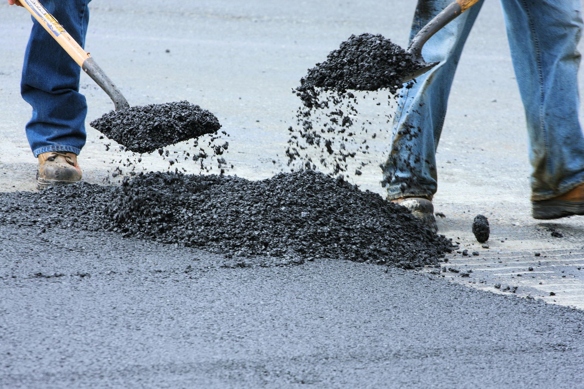Two men are spreading asphalt on a road with shovels