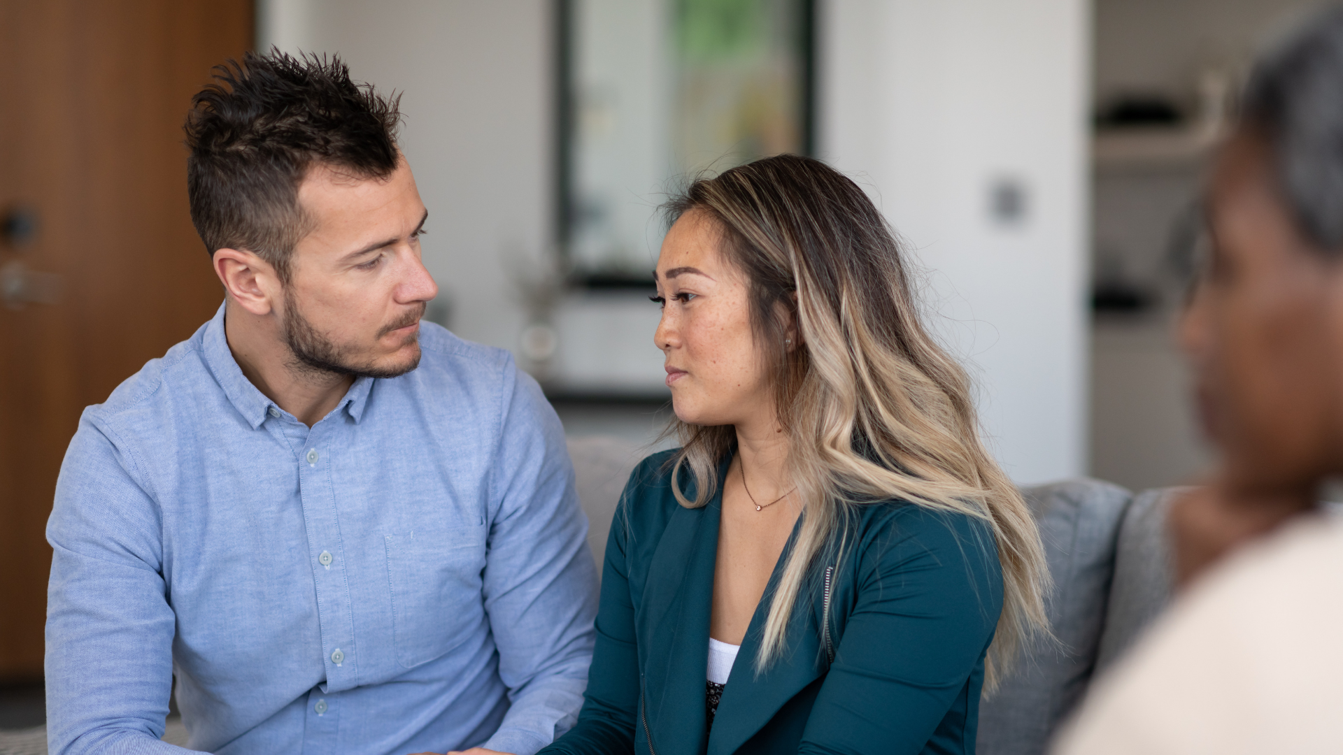 Two colleagues talking in an office, one in a blue shirt and one in a teal blazer.