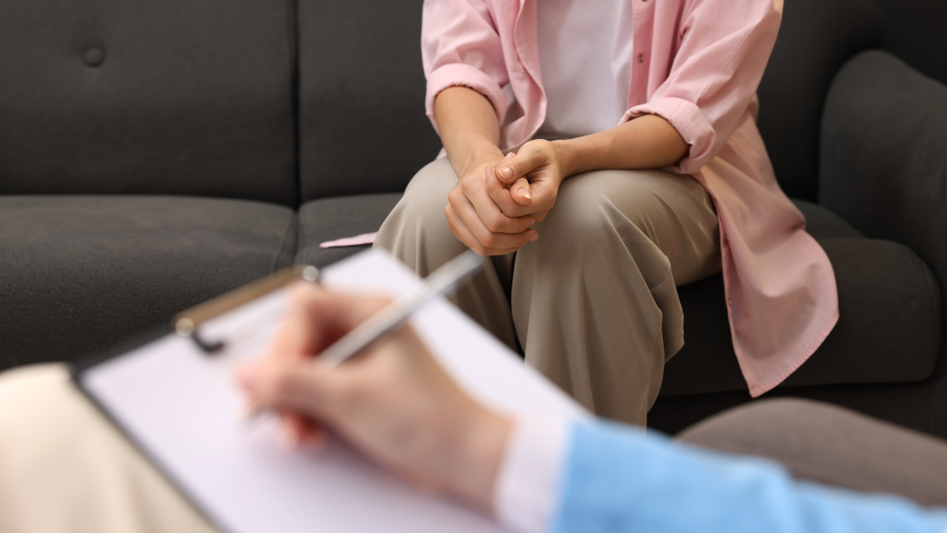 Person seated on a couch during a counseling session, with a blurred notepad in the foreground.