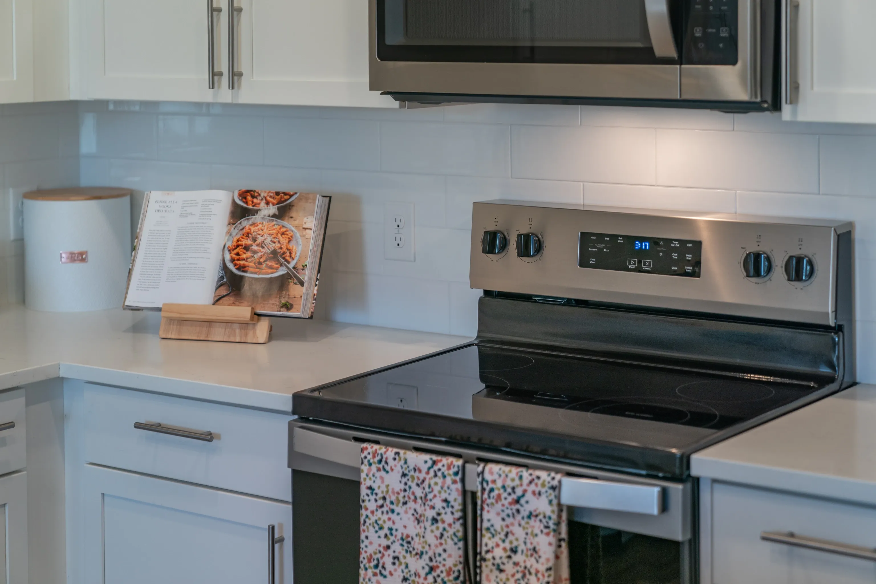 A modern kitchen features a stainless steel stove with a cookbook open on the counter.
