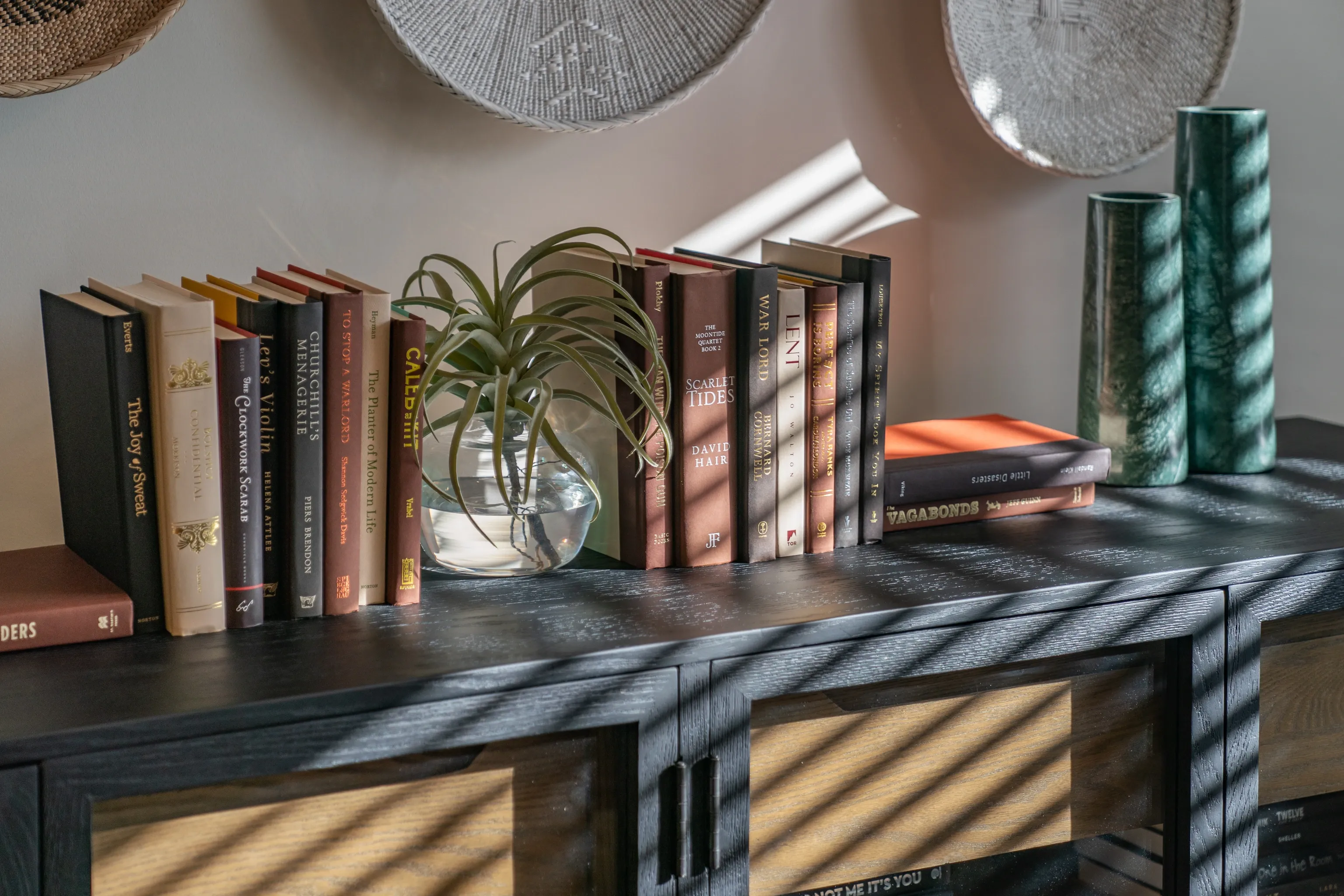 Books and decorative items on a shelf, including a plant in a glass vase.