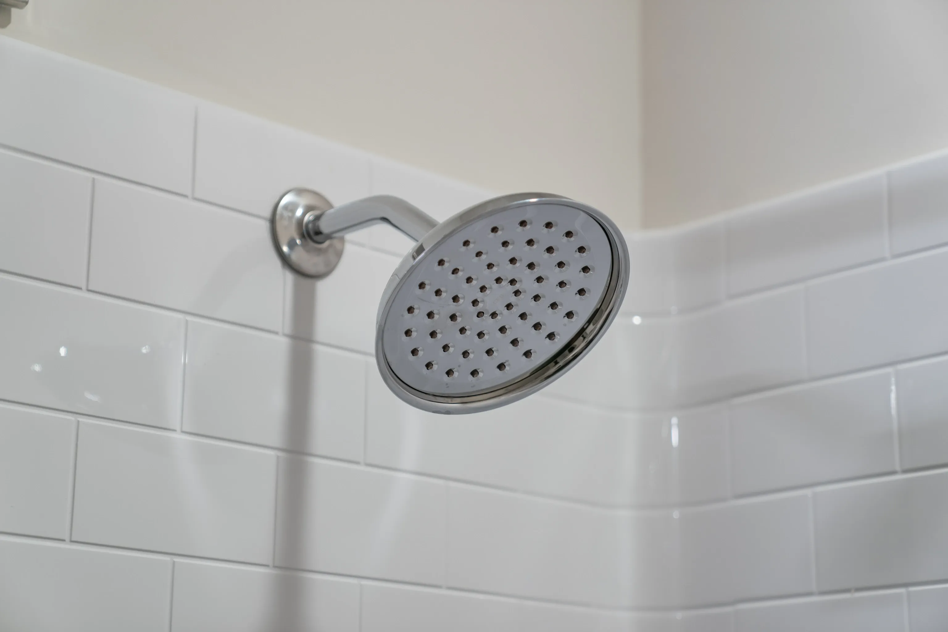 Close-up of a modern chrome shower head against white subway tiles.