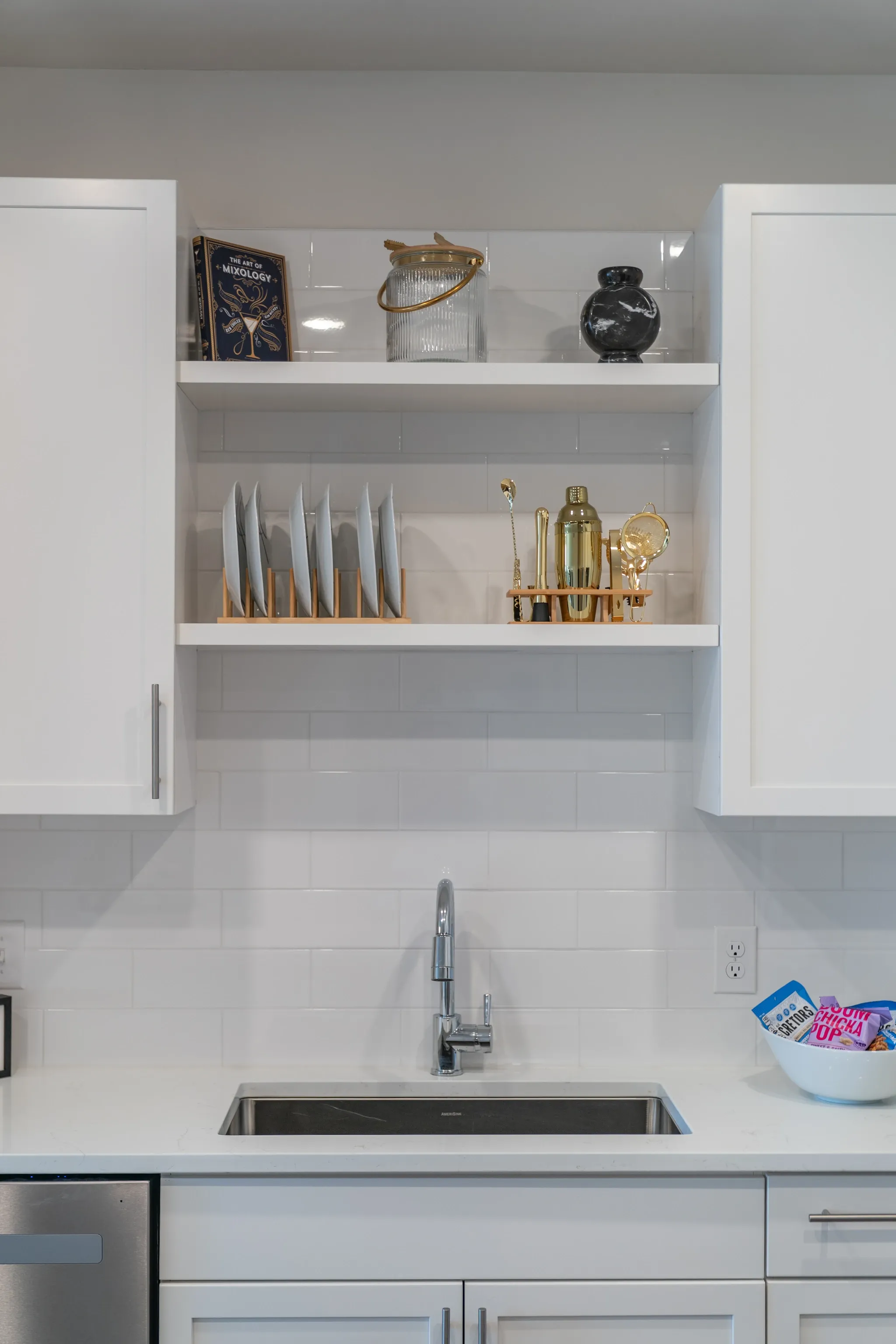 Kitchen sink area with white subway tile backsplash and open shelving with decorative items.