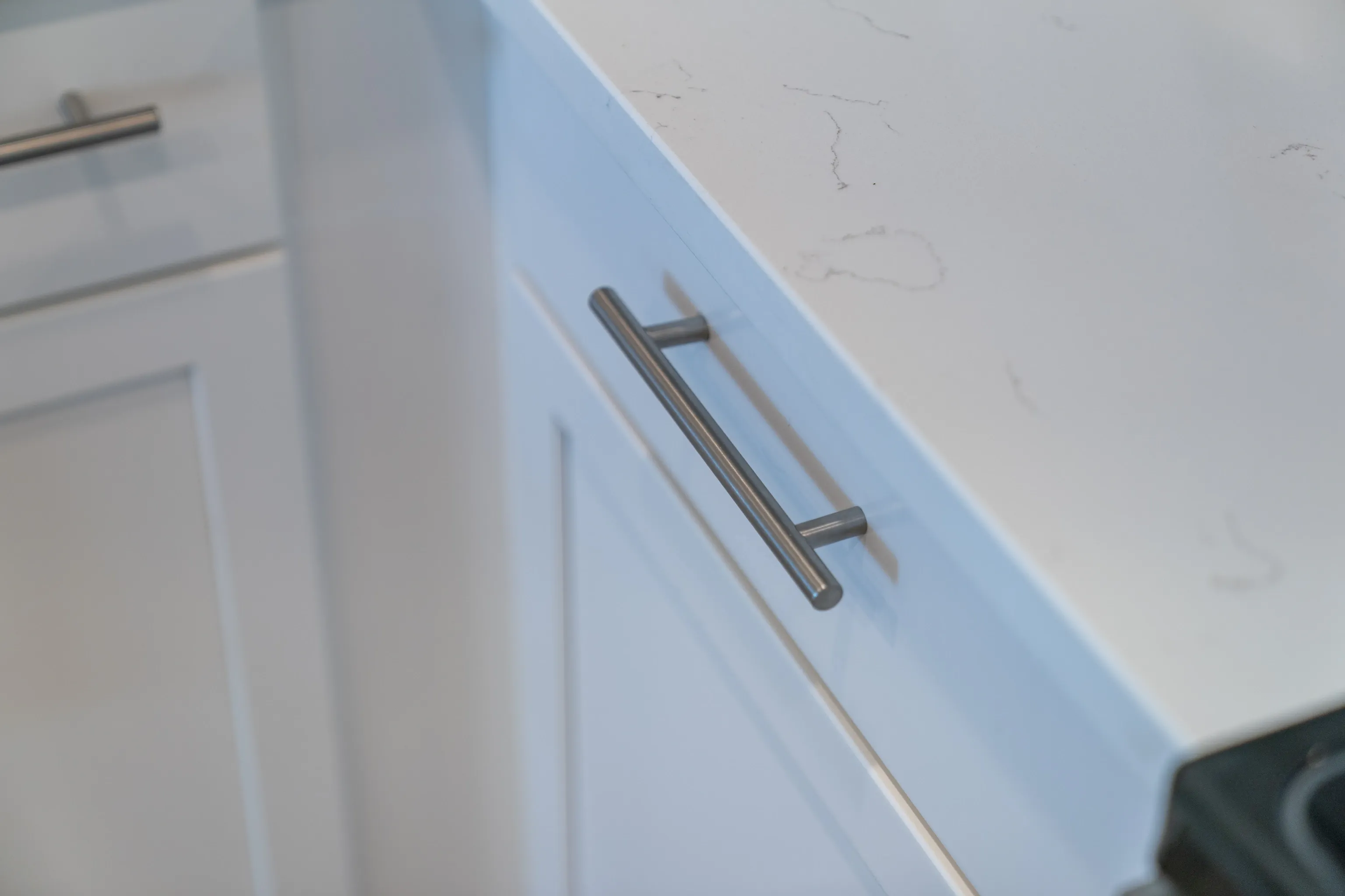 Close-up of white kitchen cabinets with brushed nickel pulls and quartz countertop.