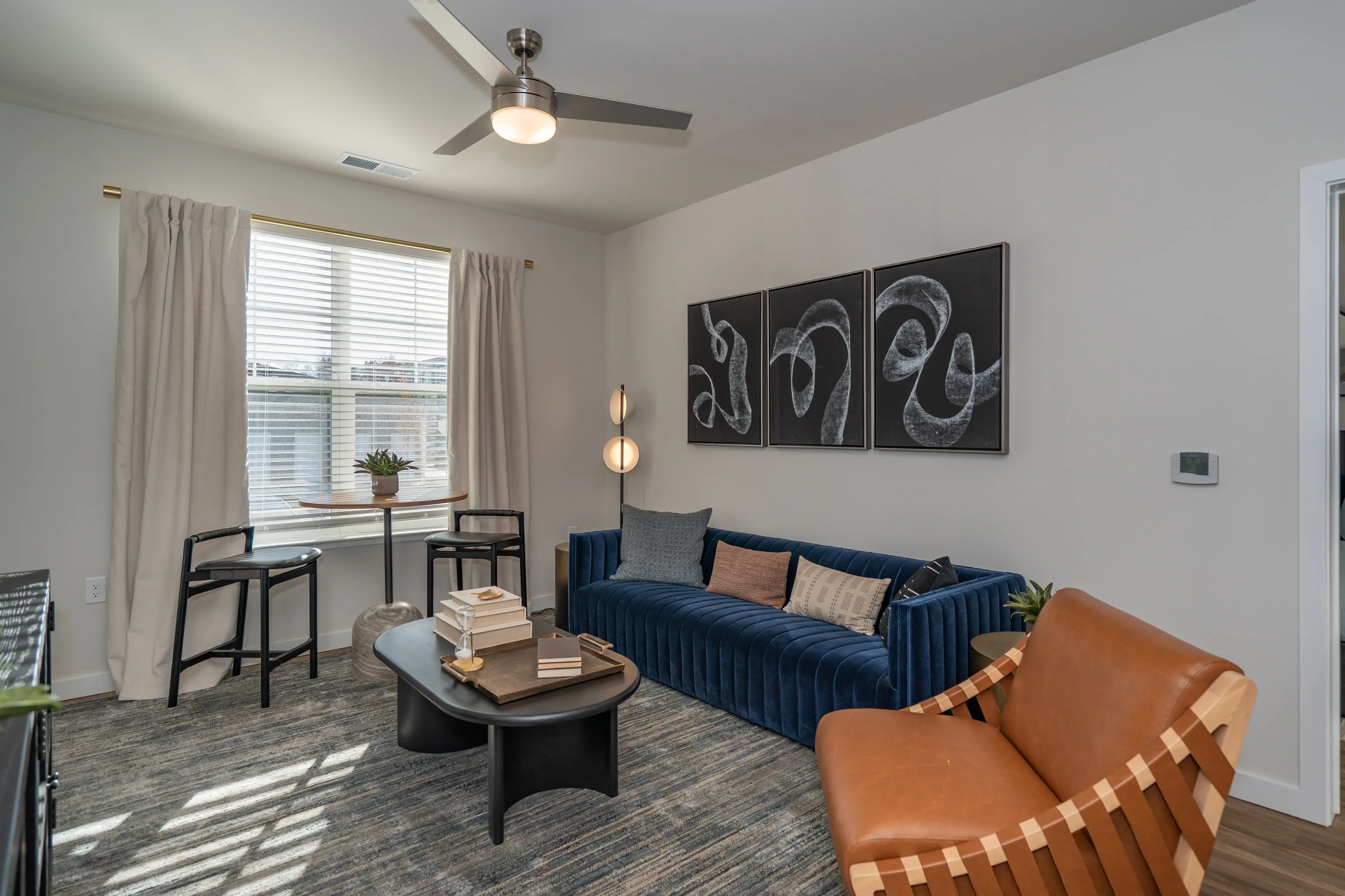 Living room with blue sofa, accent chair, coffee table, and bar stools near window.