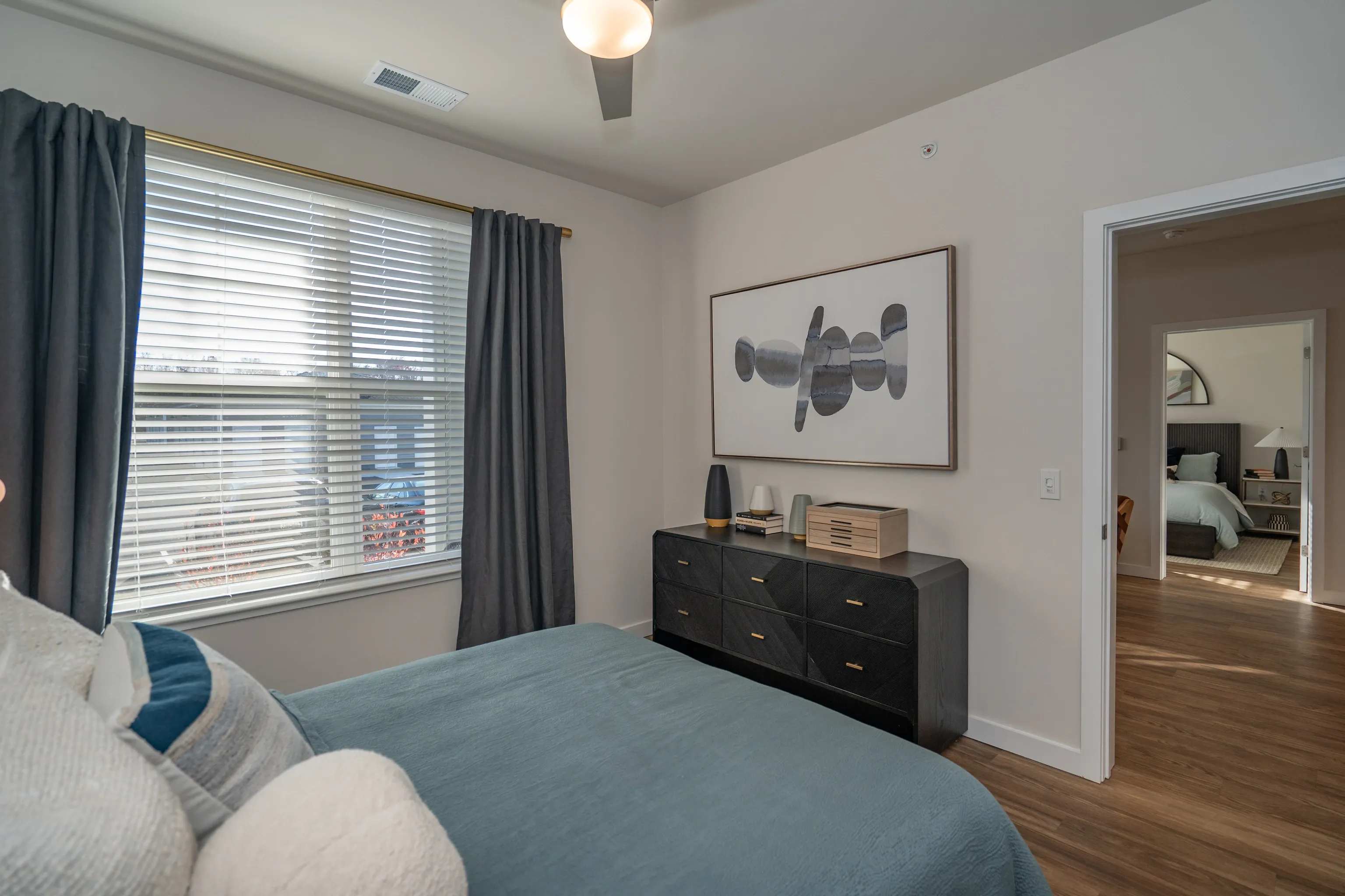 Bedroom with a bed, dresser, window with blinds, and a doorway to another room.