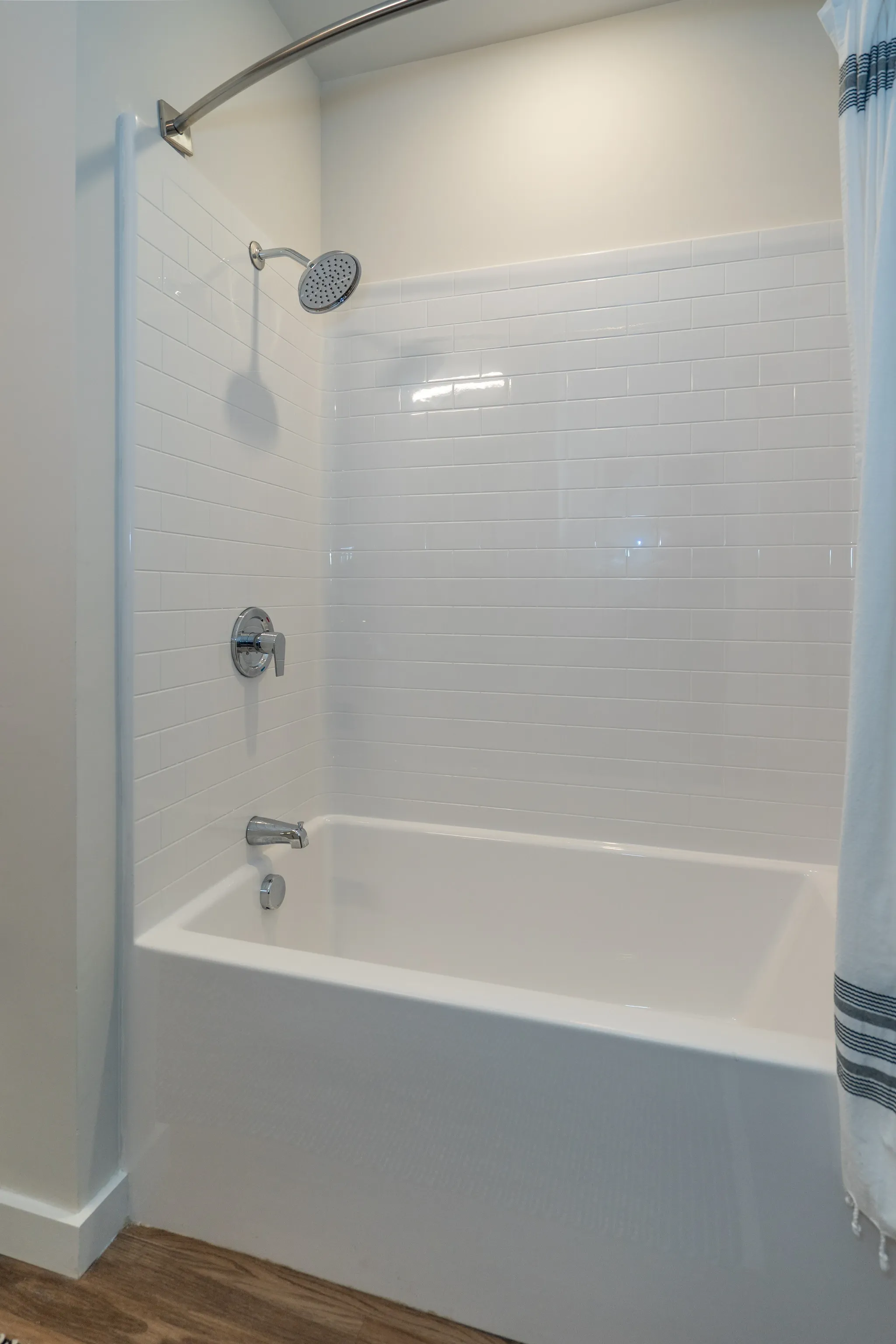 White subway tile shower surround with a chrome shower head and bathtub.