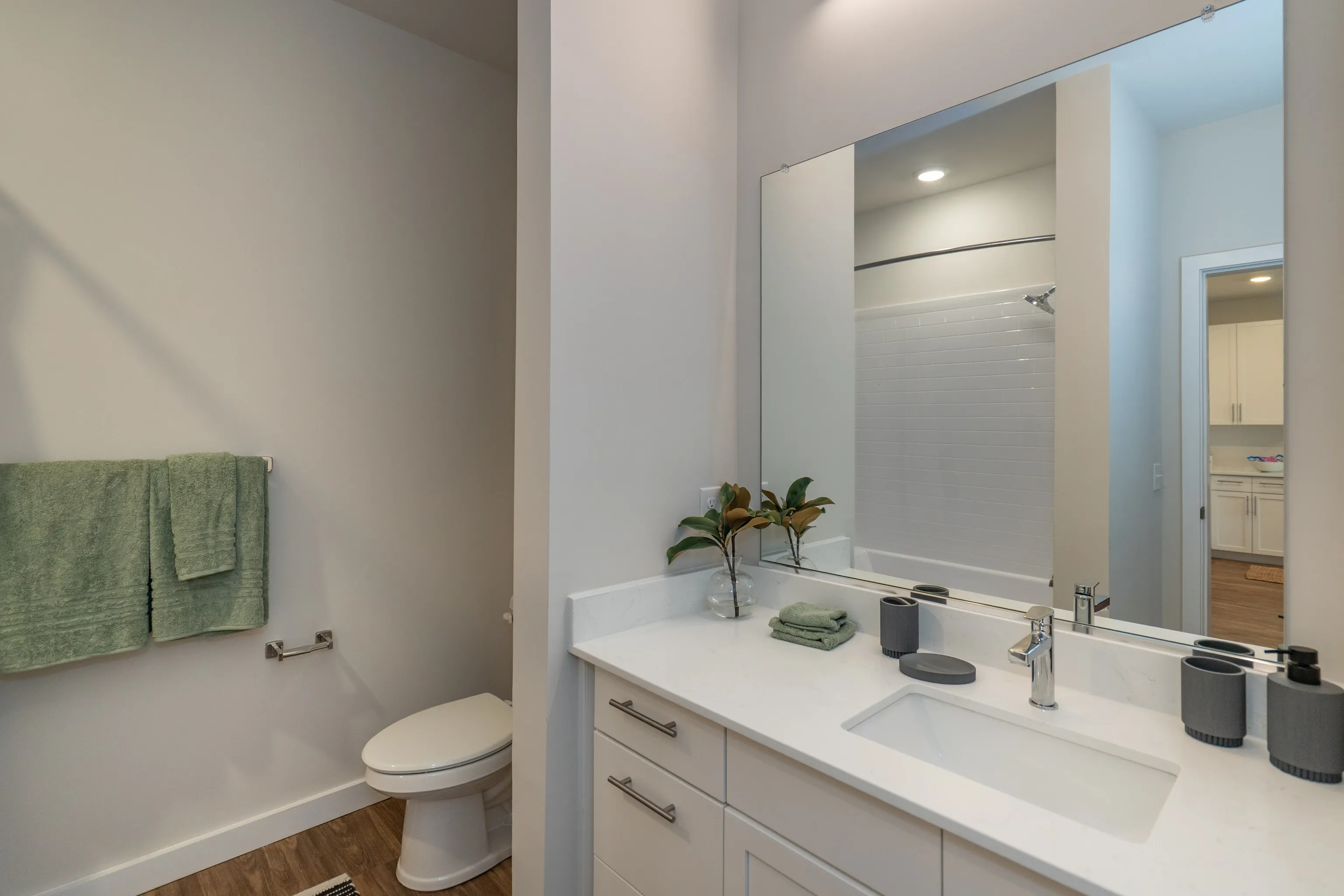 Modern bathroom with white vanity, sink, and a large mirror reflecting the shower.