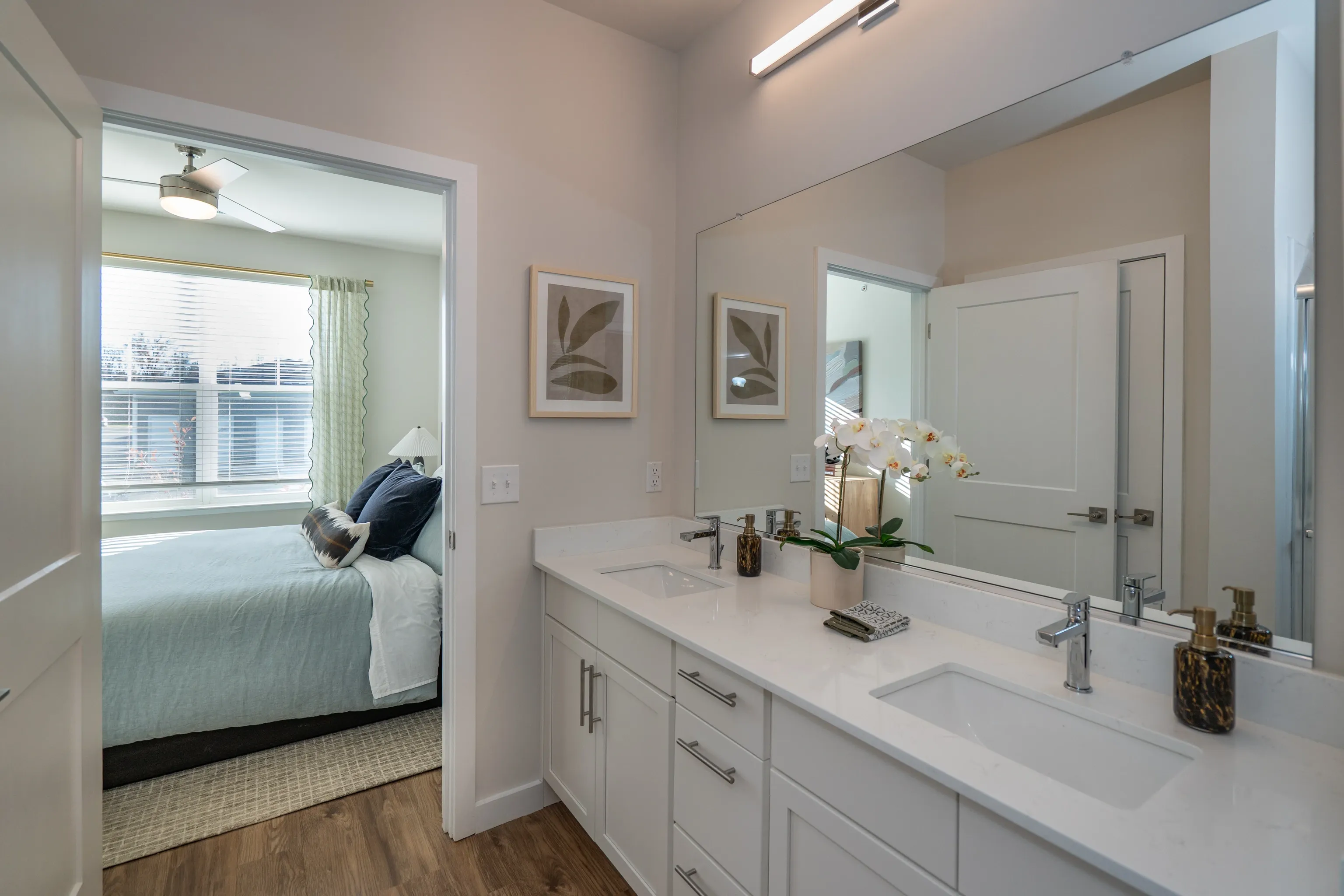 Dual vanity with white countertops and chrome faucets, overlooking a bedroom.