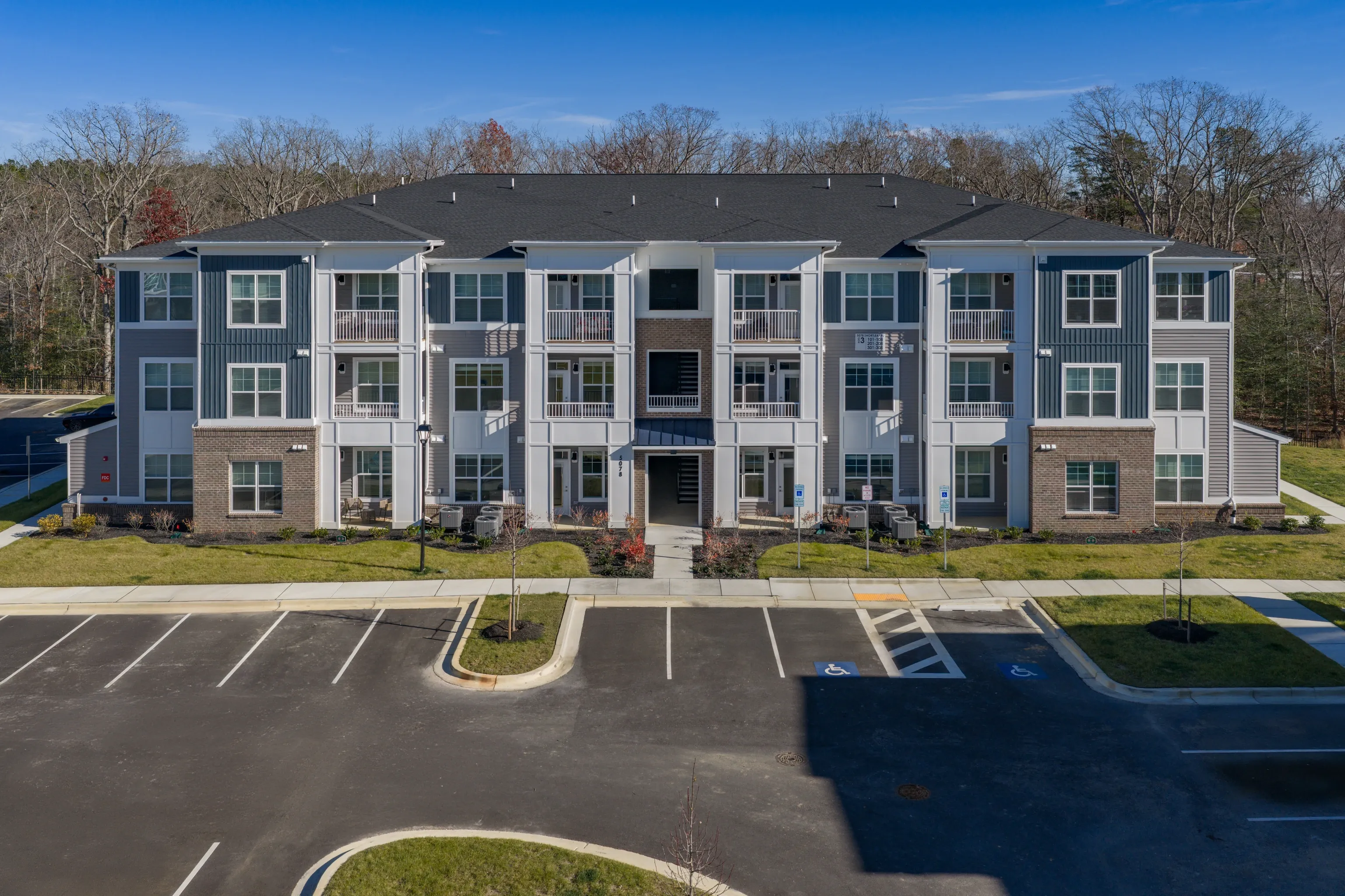 Exterior view of a modern apartment building with balconies and a parking lot.
