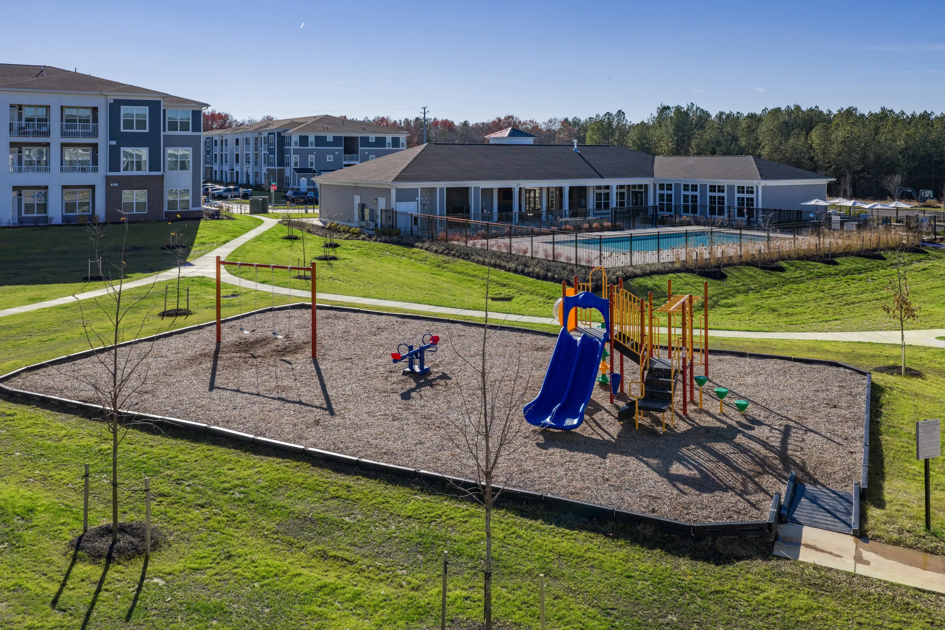Playground with slides and swings next to a swimming pool and apartment buildings.