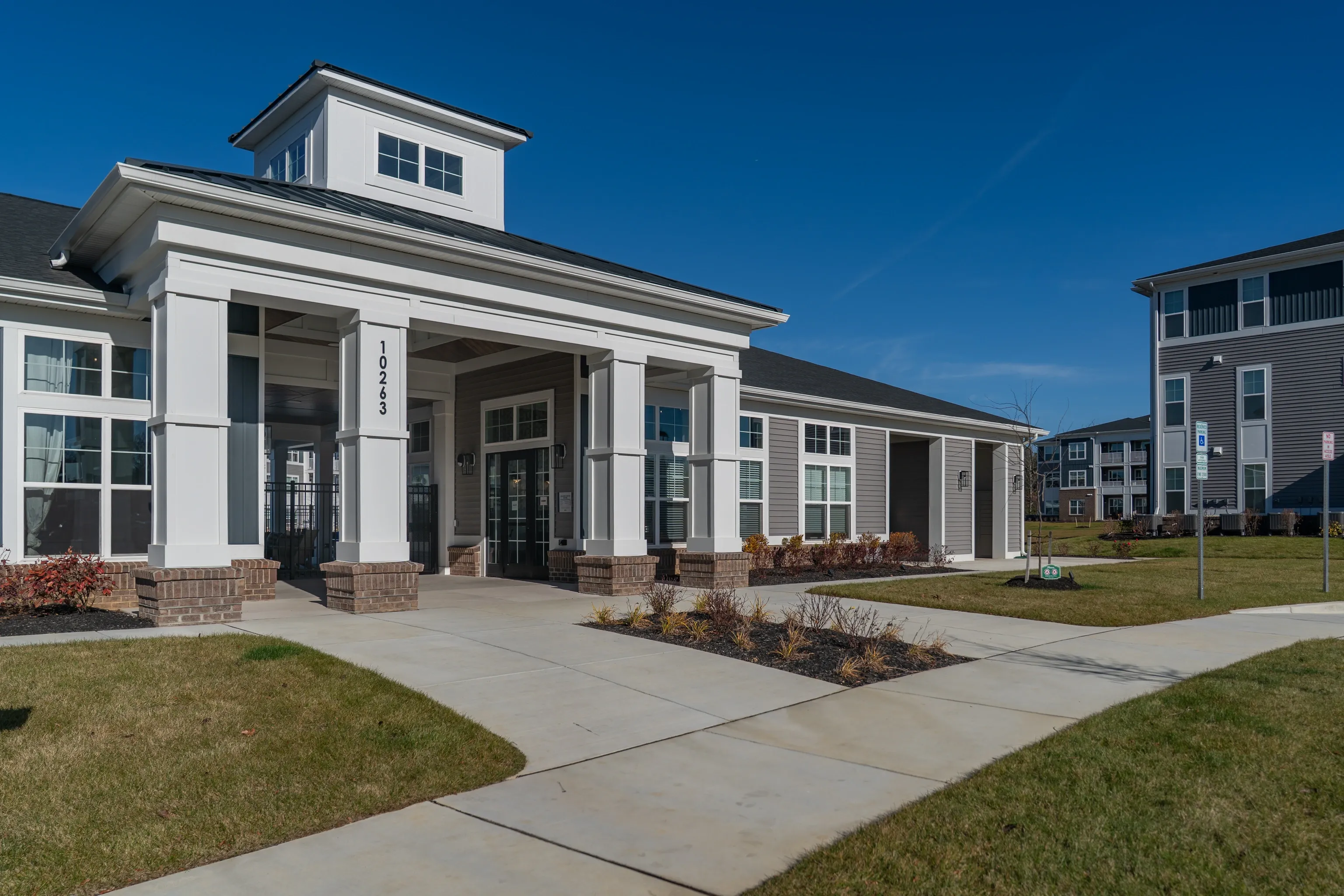 Exterior view of apartment complex clubhouse entrance with columns and windows.