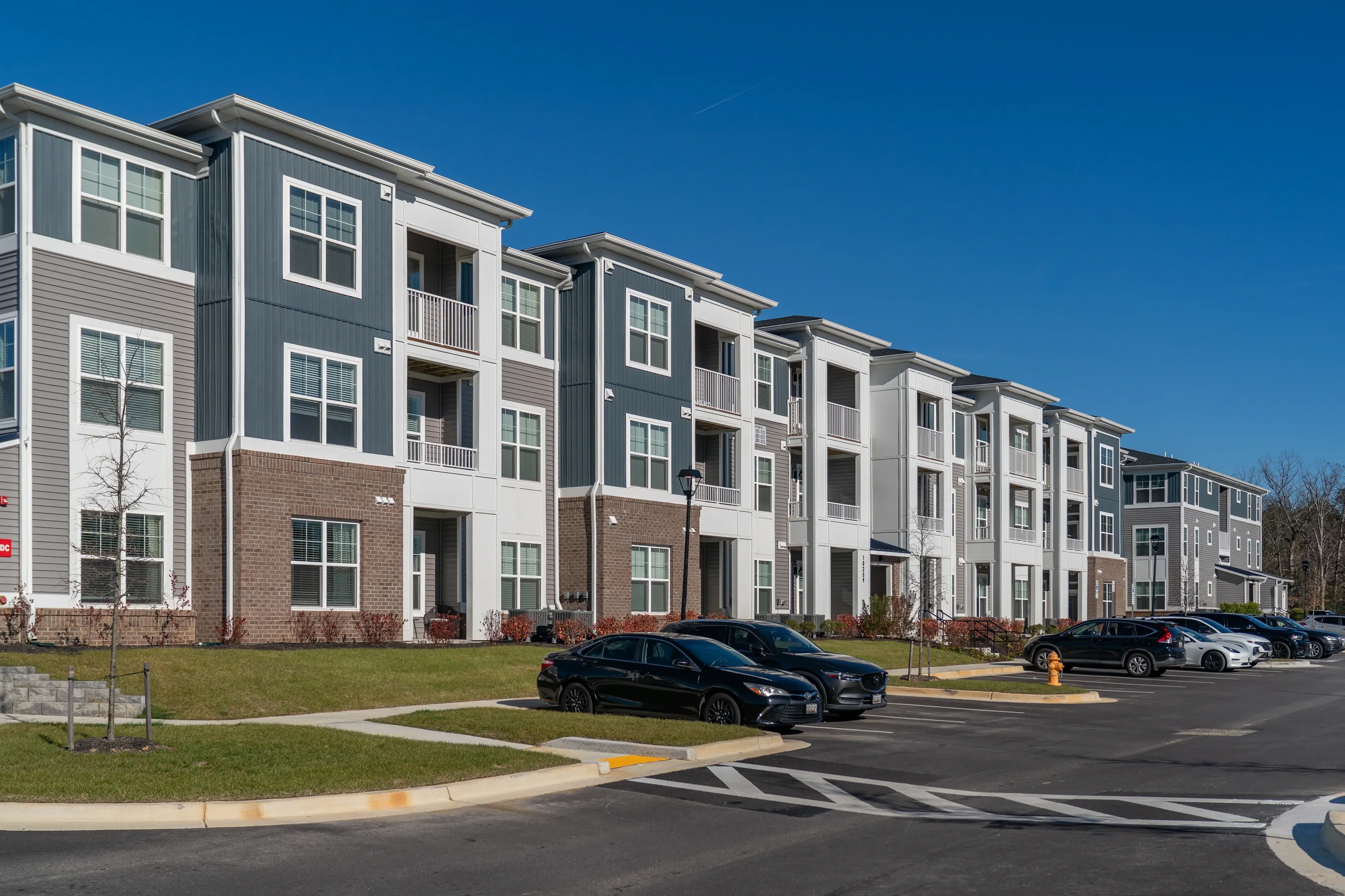 Exterior view of a modern apartment building with balconies and a parking lot.