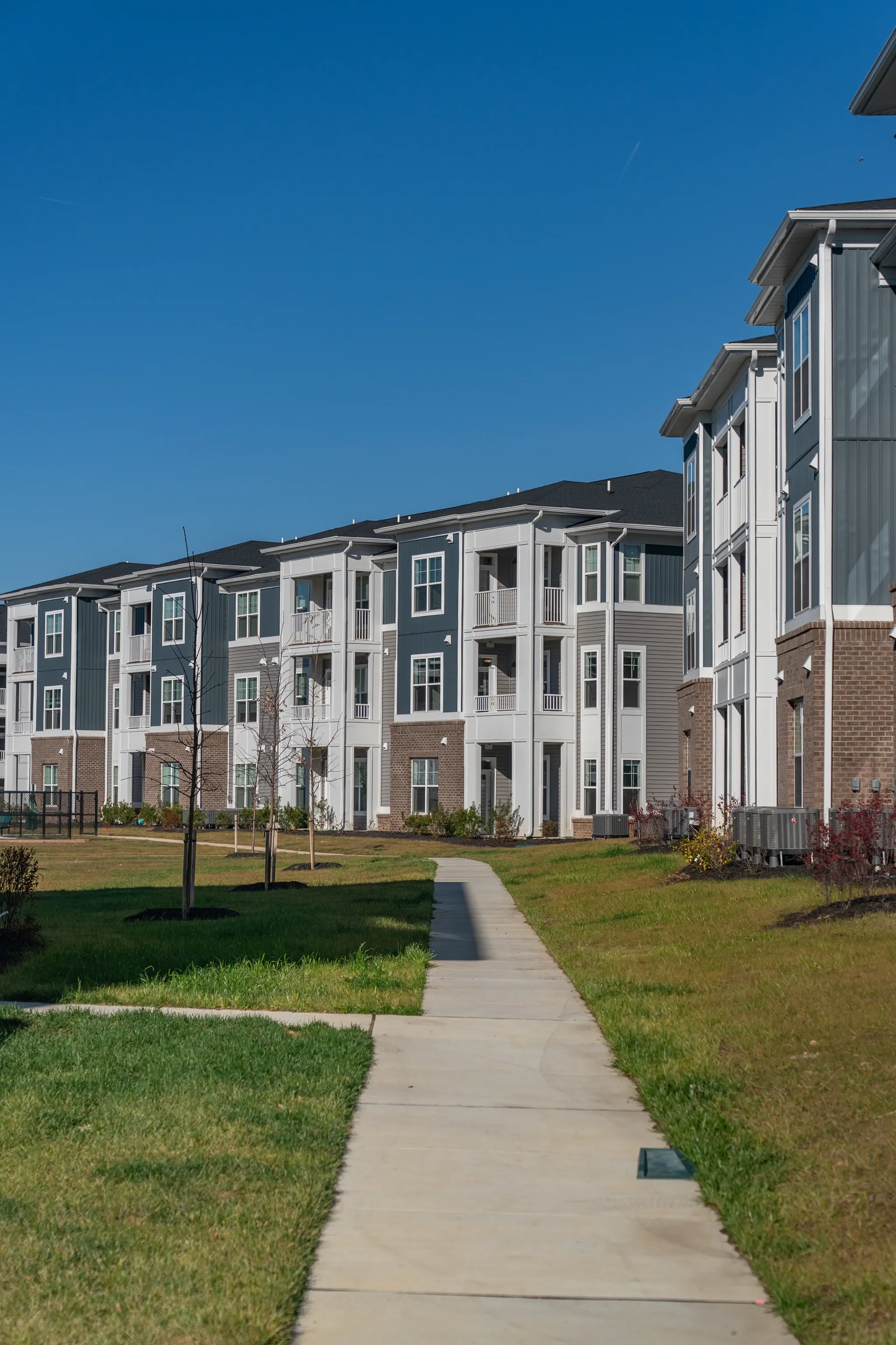 Exterior view of modern apartment buildings with a walking path leading towards them on a sunny day.